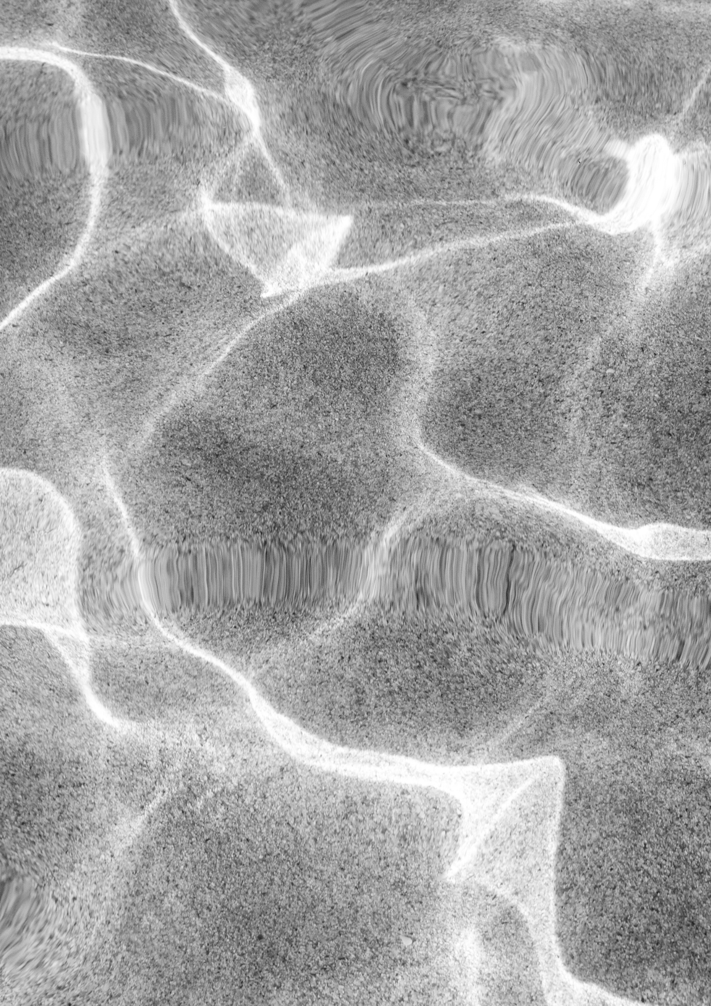 Close-up of wet sand with light reflections creating patterns and ripples.