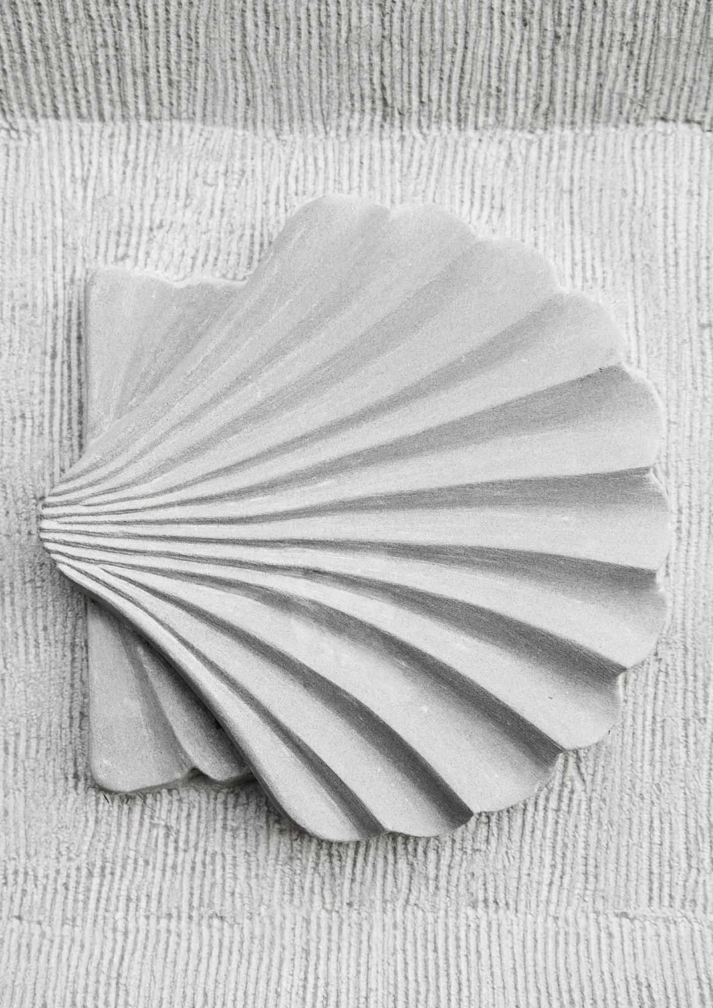 A decorative ceramic shell wall sculpture with a fan shape, featuring carved linear ridges, mounted on a textured wall.