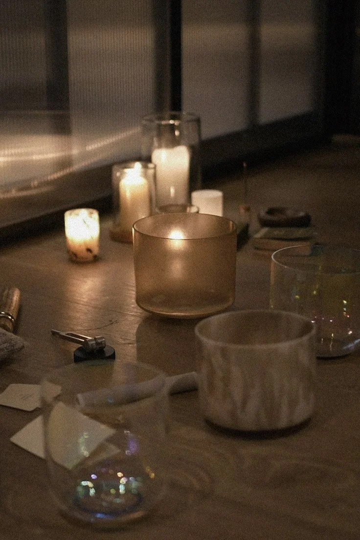 A cozy table setting with lit candles, a small glass cup, pens, and papers on a wooden surface.