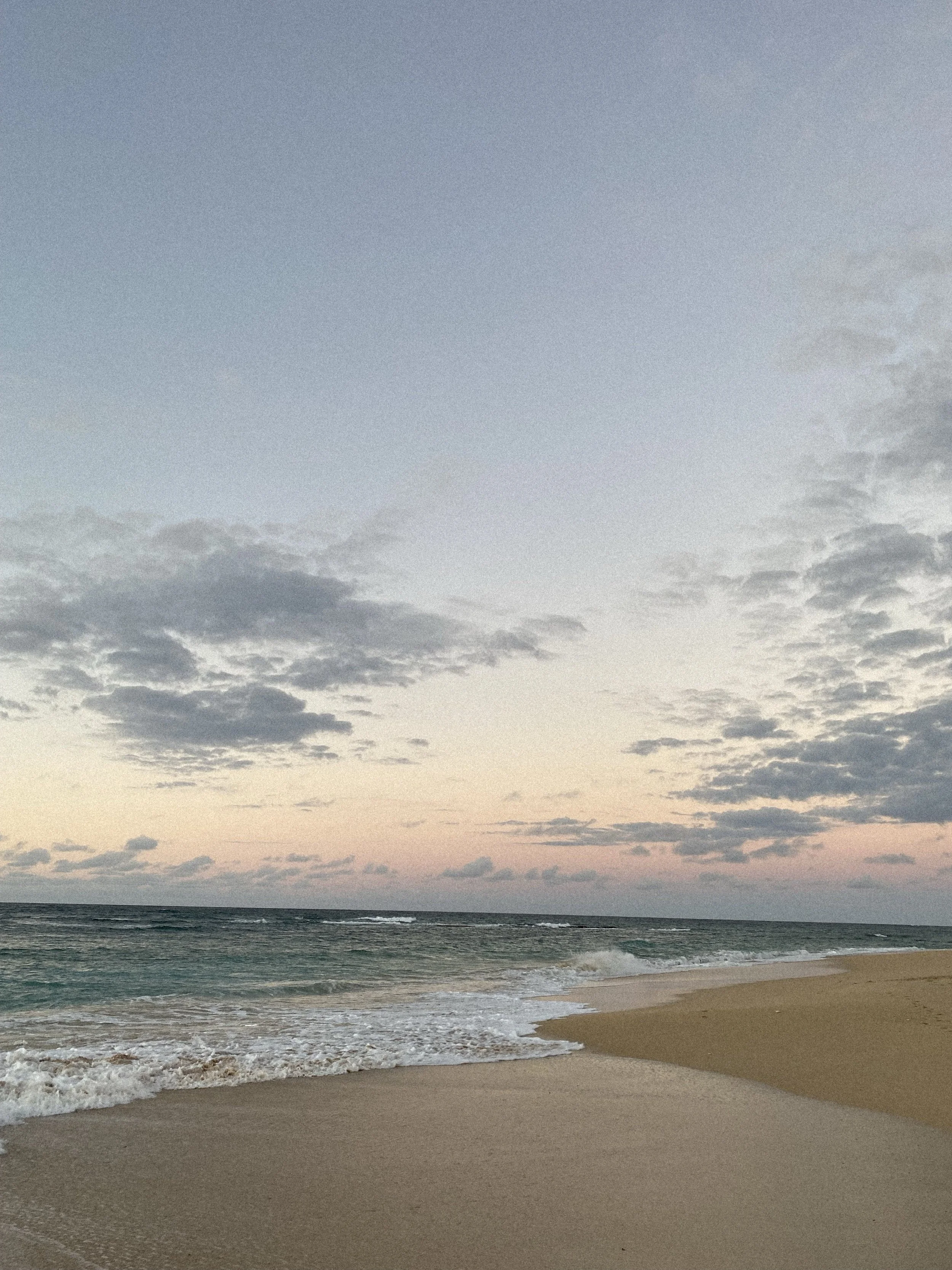 A peaceful beach scene during sunset, showing the ocean waves gently lapping the sandy shore with clouds in the sky.