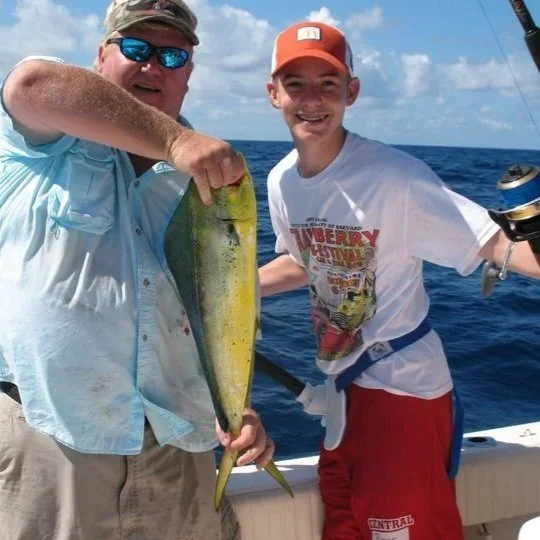Two men on a boat at sea holding a large fish, smiling for the camera.