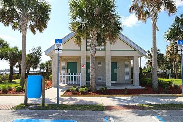 Public restroom building surrounded by palm trees, with handicapped parking signs and parking spaces in front.