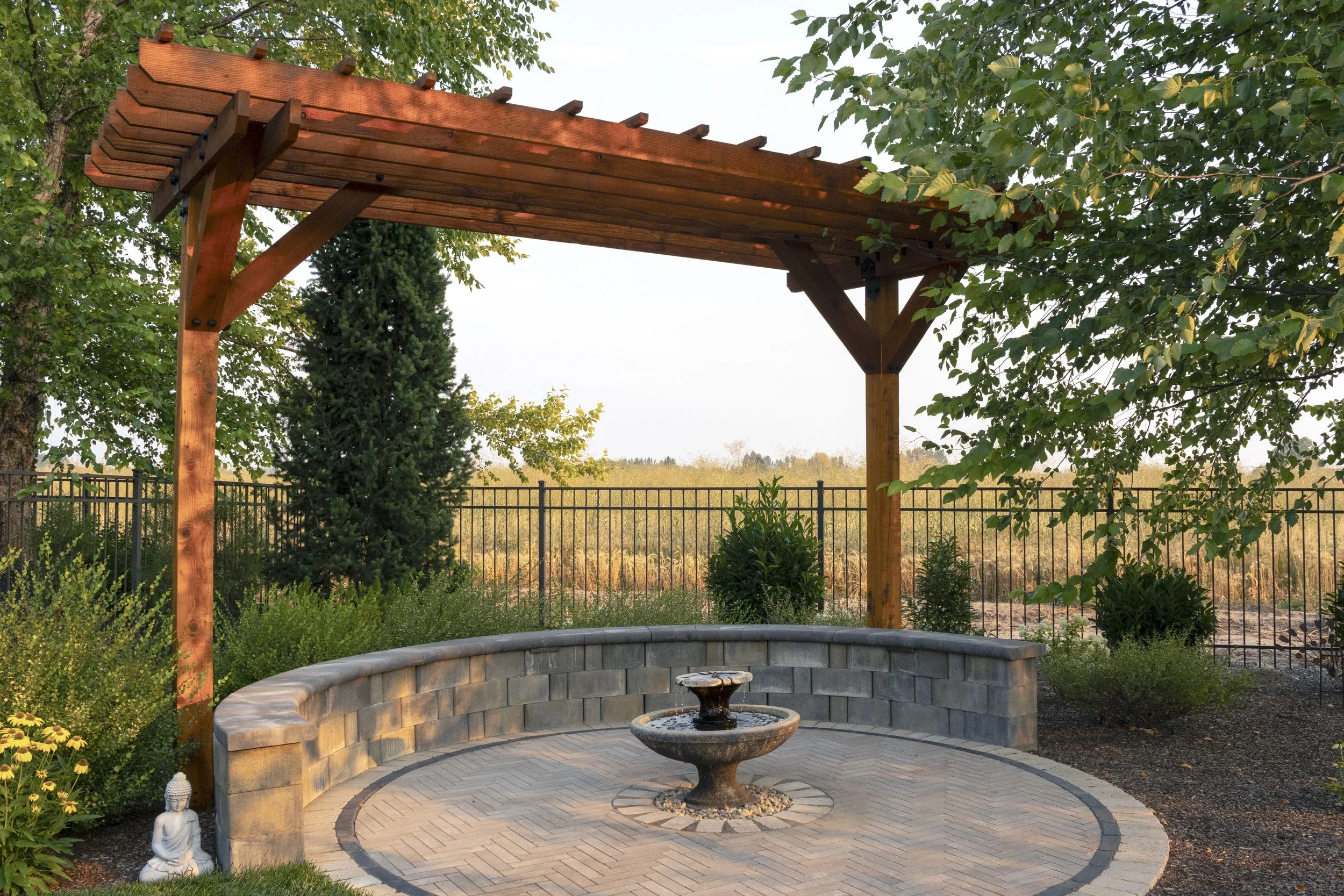 Custom landscape design in Eagle, Idaho featuring a shaded pergola, natural stone seating wall, and elegant water feature designed for outdoor gathering.