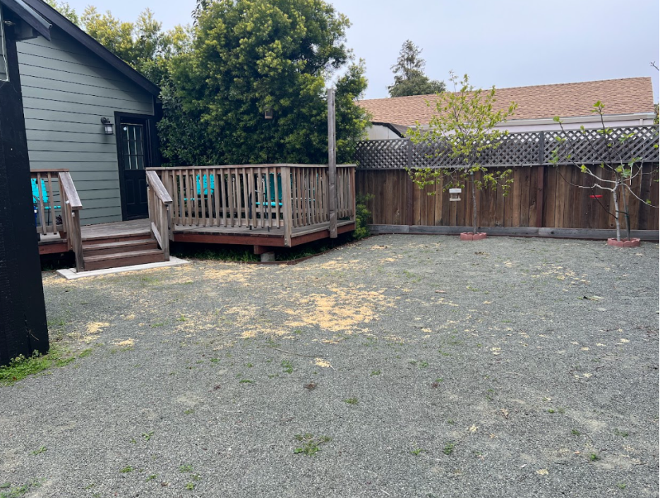 Backyard with a small wooden deck, two trees, a wooden fence, and a gravel ground.
