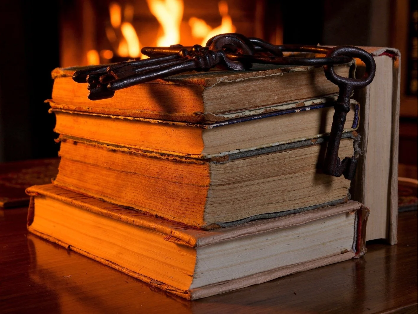 Stack of old books with a set of antique keys on top, placed in front of a fireplace.