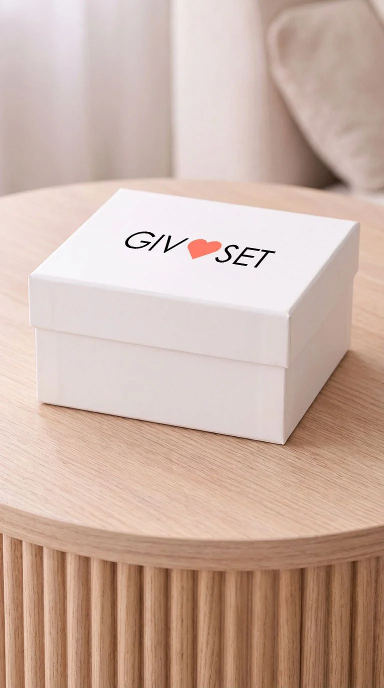 A white gift box with a lid sitting on a wooden table. The box has the words "GIFT SET" with a red heart symbol replacing the letter "O" in "LOVE."
