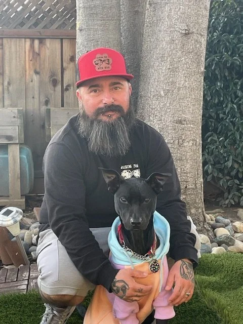 Ryan De Luca, professional dog walker and pet sitter in San Mateo, CA, sitting outdoors next to a black dog.