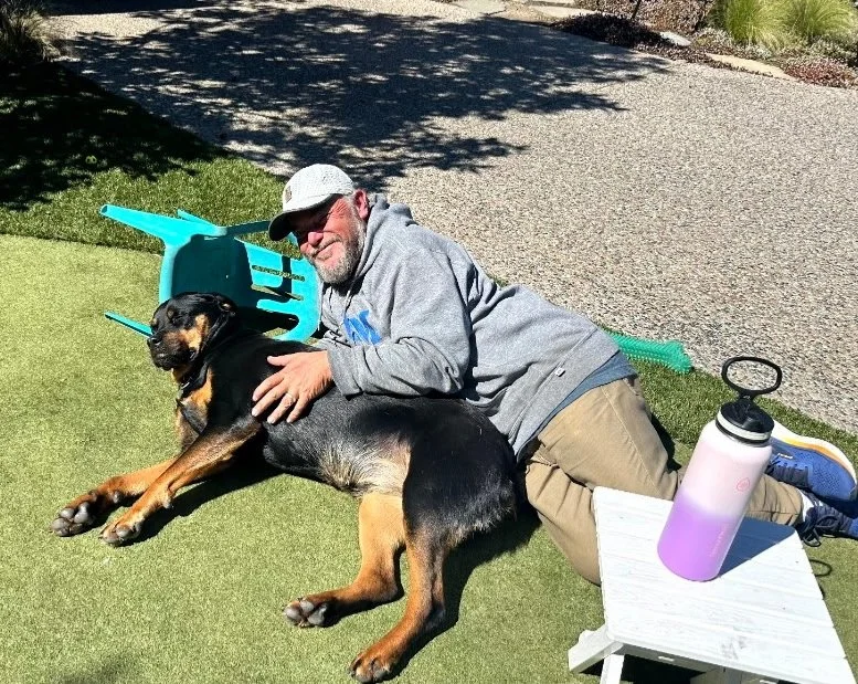 Walking Paws with Ryan dog walker relaxing on grass outdoors with a large Rottweiler during a boarding stay in San Mateo.
