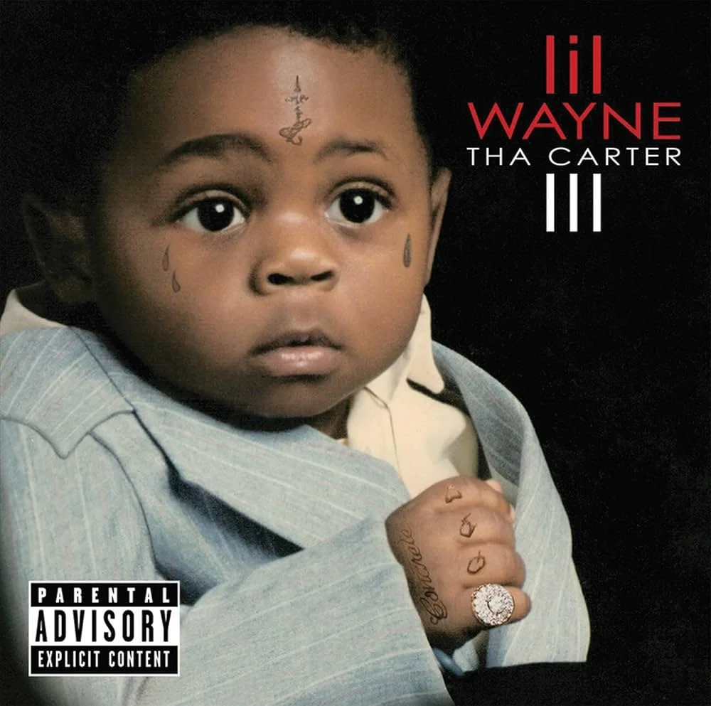 Close-up of a young child with tattoos on face and hand, wearing a gray blazer, with album title "Lil Wayne Tha Carter III" and parental advisory label on the cover.