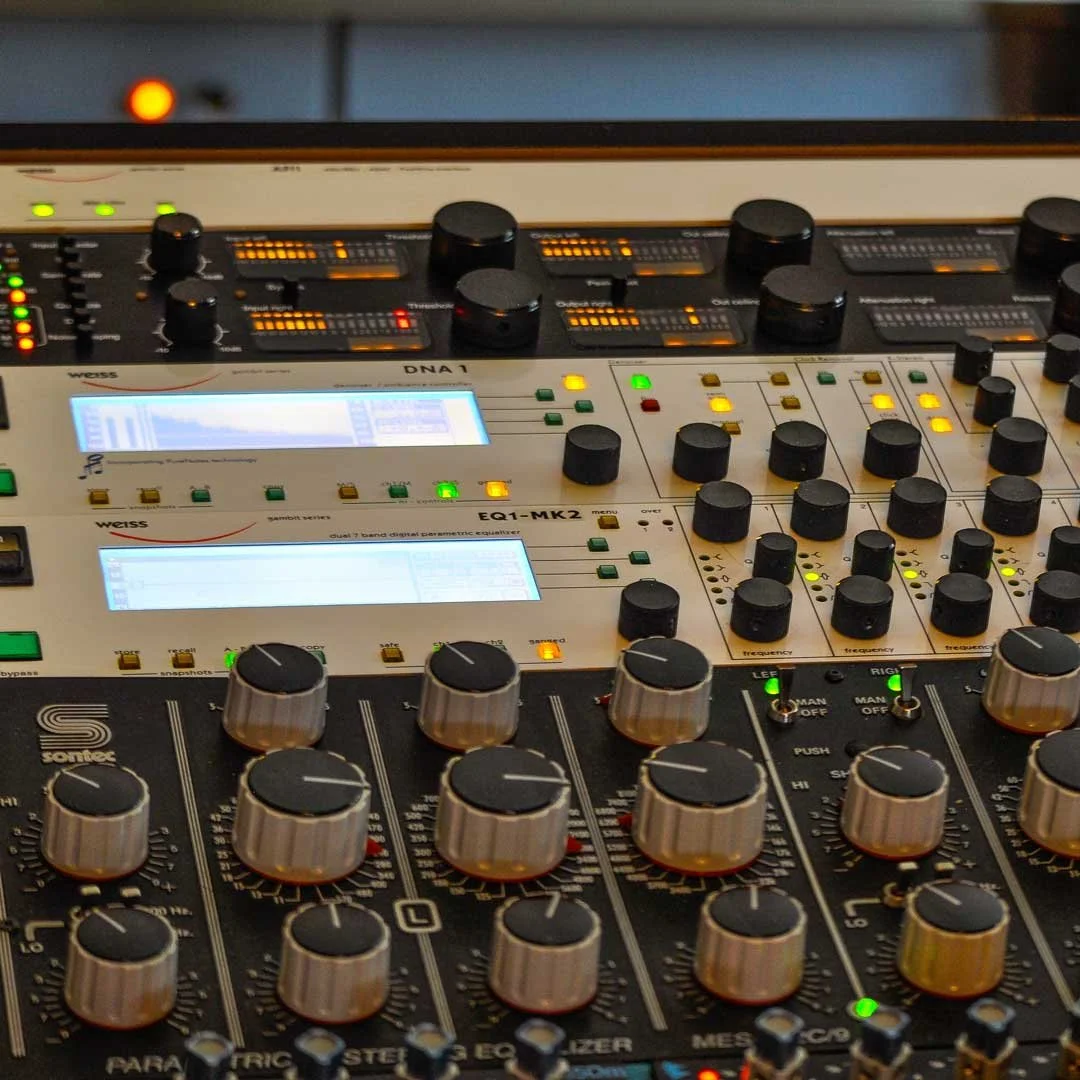 Close-up of a professional audio mixing console with various knobs, sliders, and digital displays.