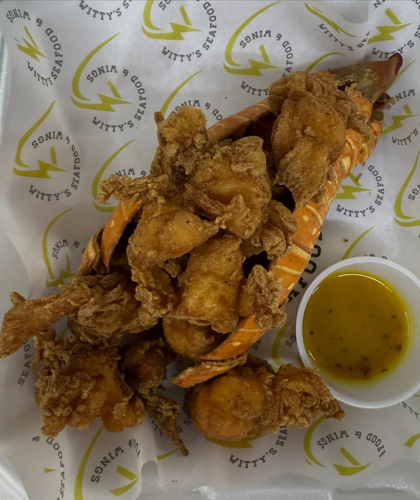 A serving of fried seafood in a lobster shell, with fried fish and chicken pieces, served with a cup of dipping sauce.