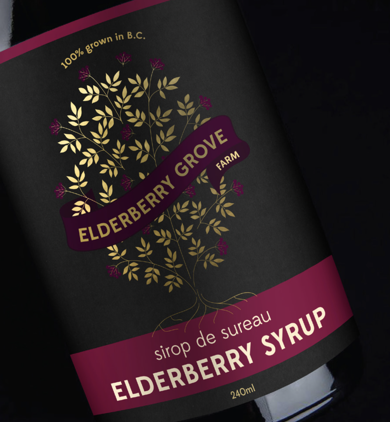 Label for Elderberry Grove Farm elderberry syrup featuring a black background with gold and purple leaf and flower illustrations, and gold and purple text indicating the product is 100% grown in B.C.