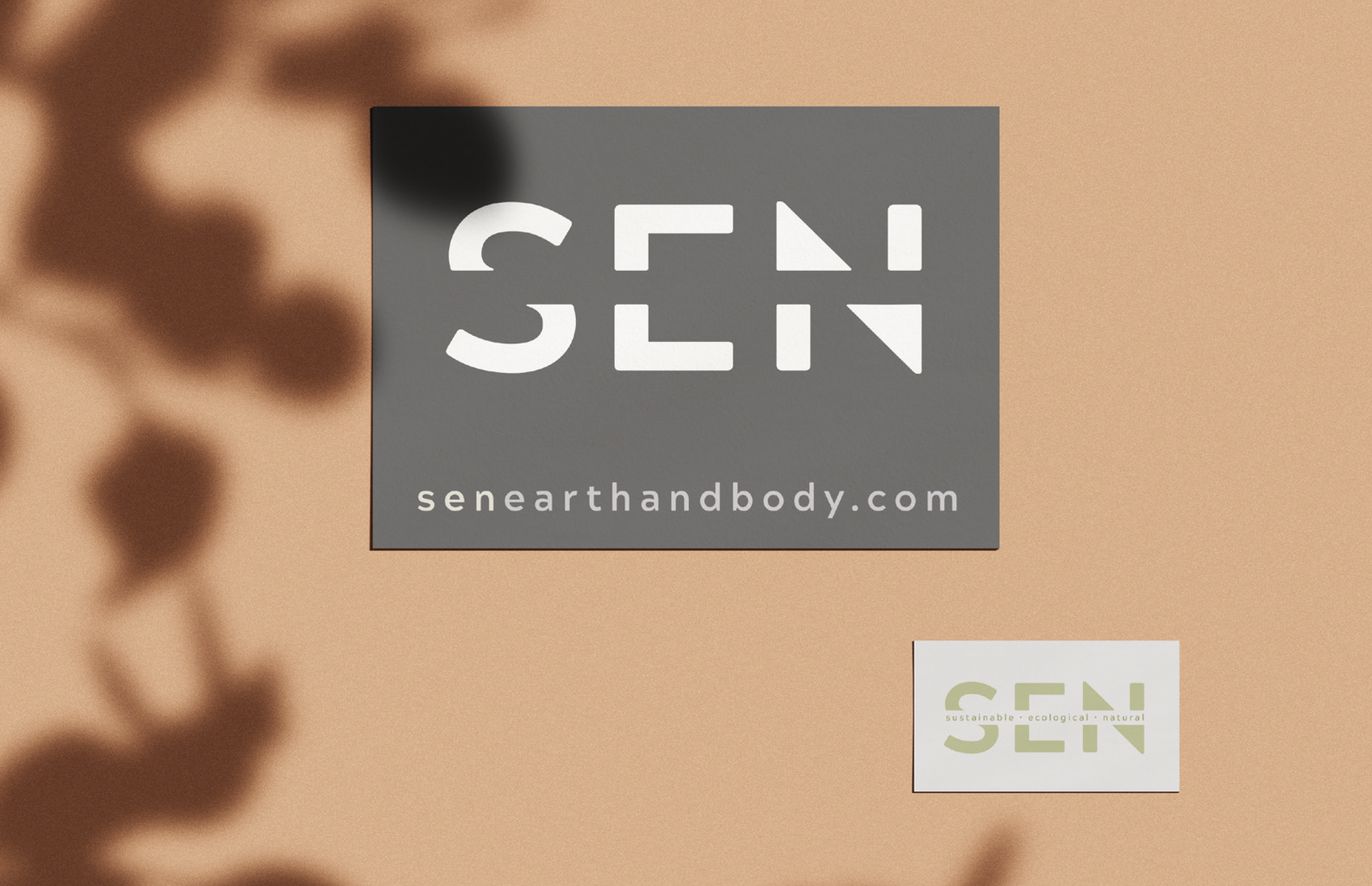 Two logo designs on a beige background for SENEARTHANDBODY.com. The larger logo features the word 'SEN' in white on a gray square with a cut-out style typography. The smaller logo below has the same word 'SEN' in green with the words 'sustainable,' 'ecological,' and 'natural' beneath it in smaller font.