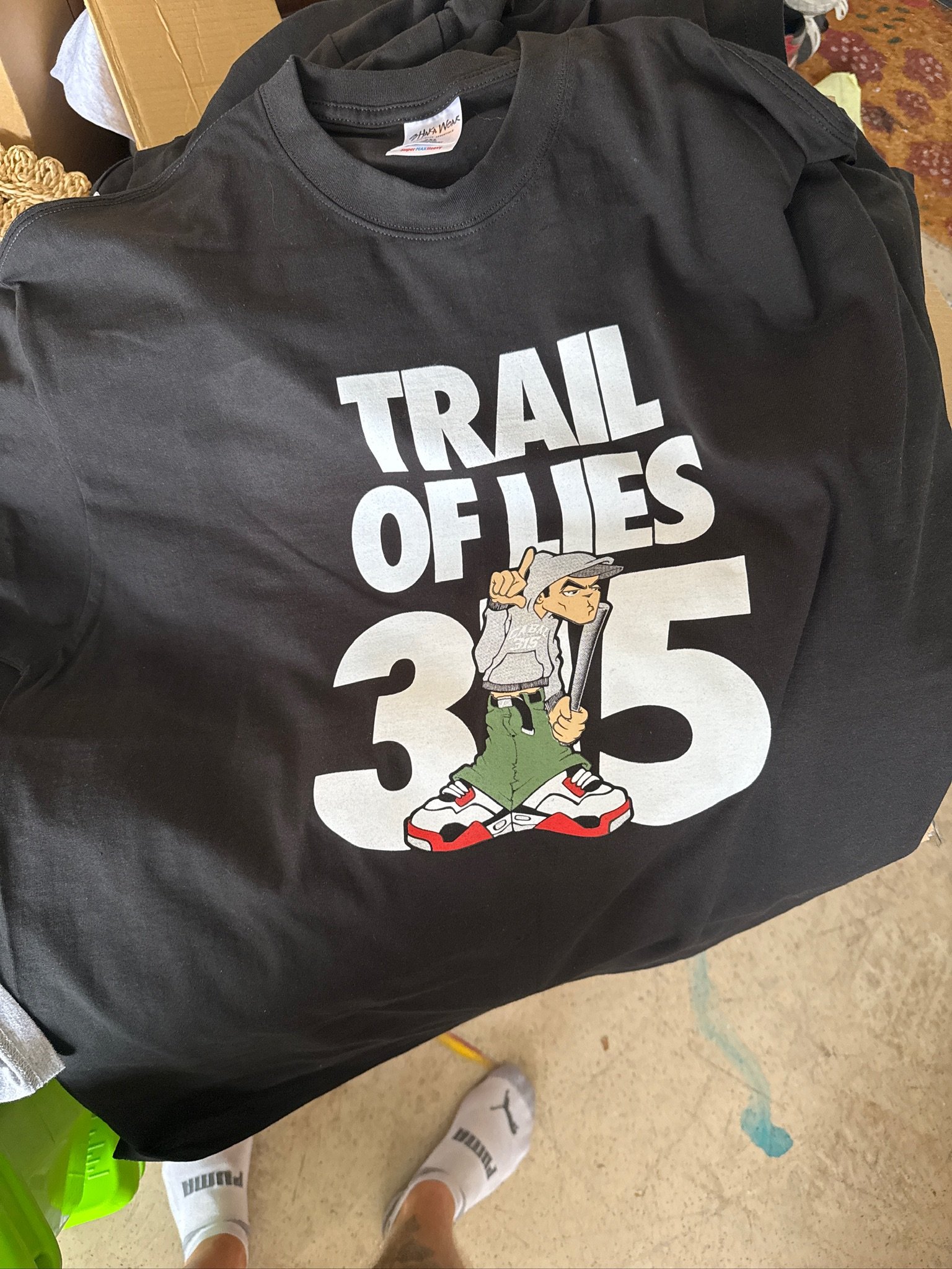 Black sweatshirt with a graphic of a cartoon boy in a hoodie and sneakers, holding a baseball bat, with text that reads 'Trail of Lies 35'.