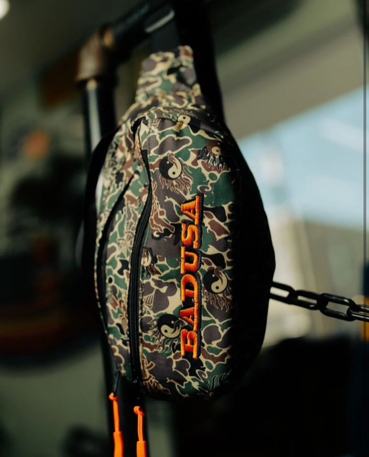 Camouflage Ed Hardy fanny pack with orange lettering hanging on a black hook.