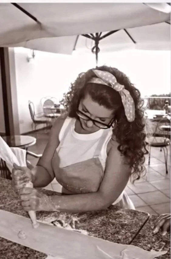A woman with curly hair, wearing glasses and a polka dot headband, is making homemade ravioli in an outdoor kitchen on the island of Capri.