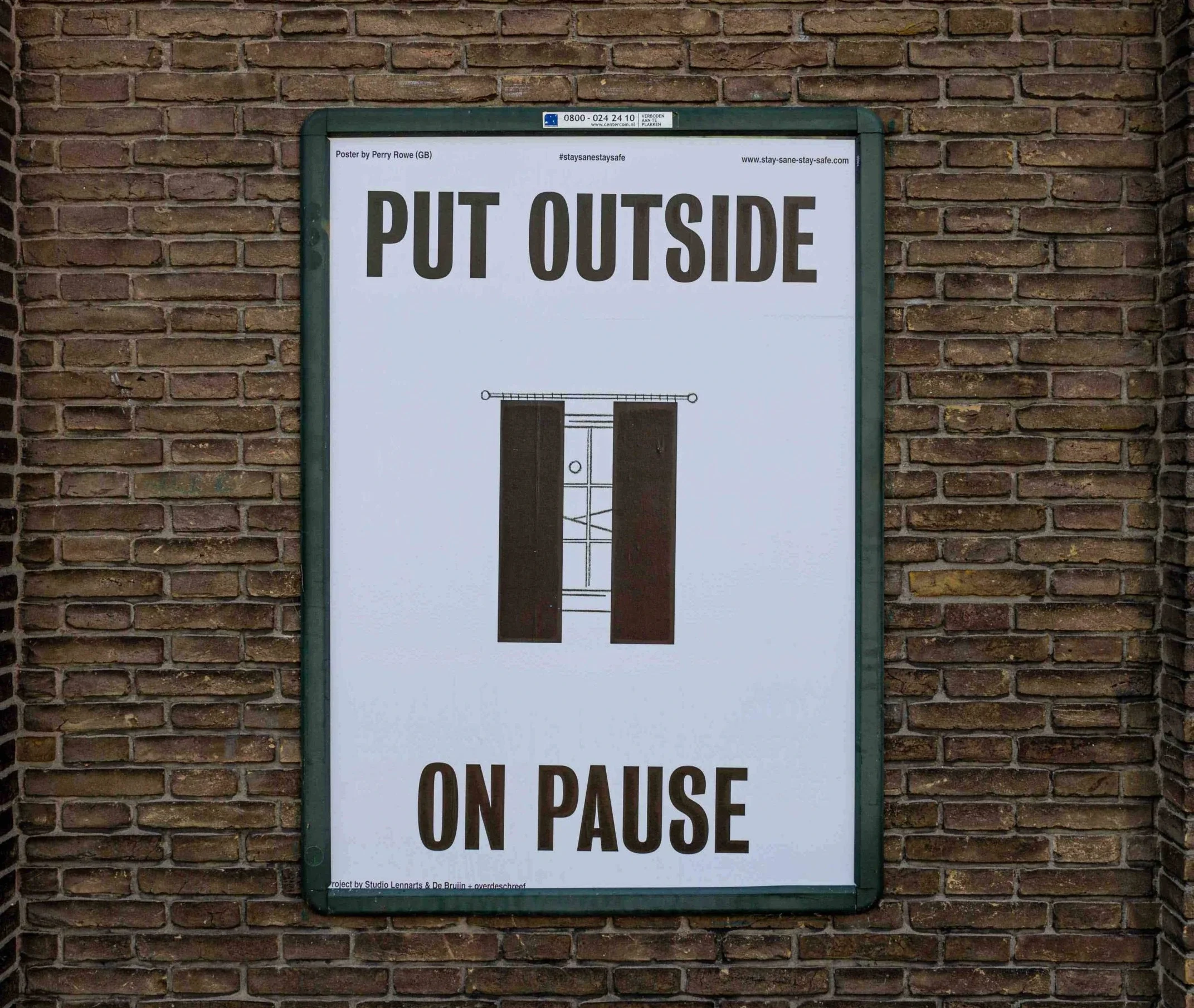 Sign on brick wall instructing to "Put Outside" and "On Pause" with a visual of a window with curtains.