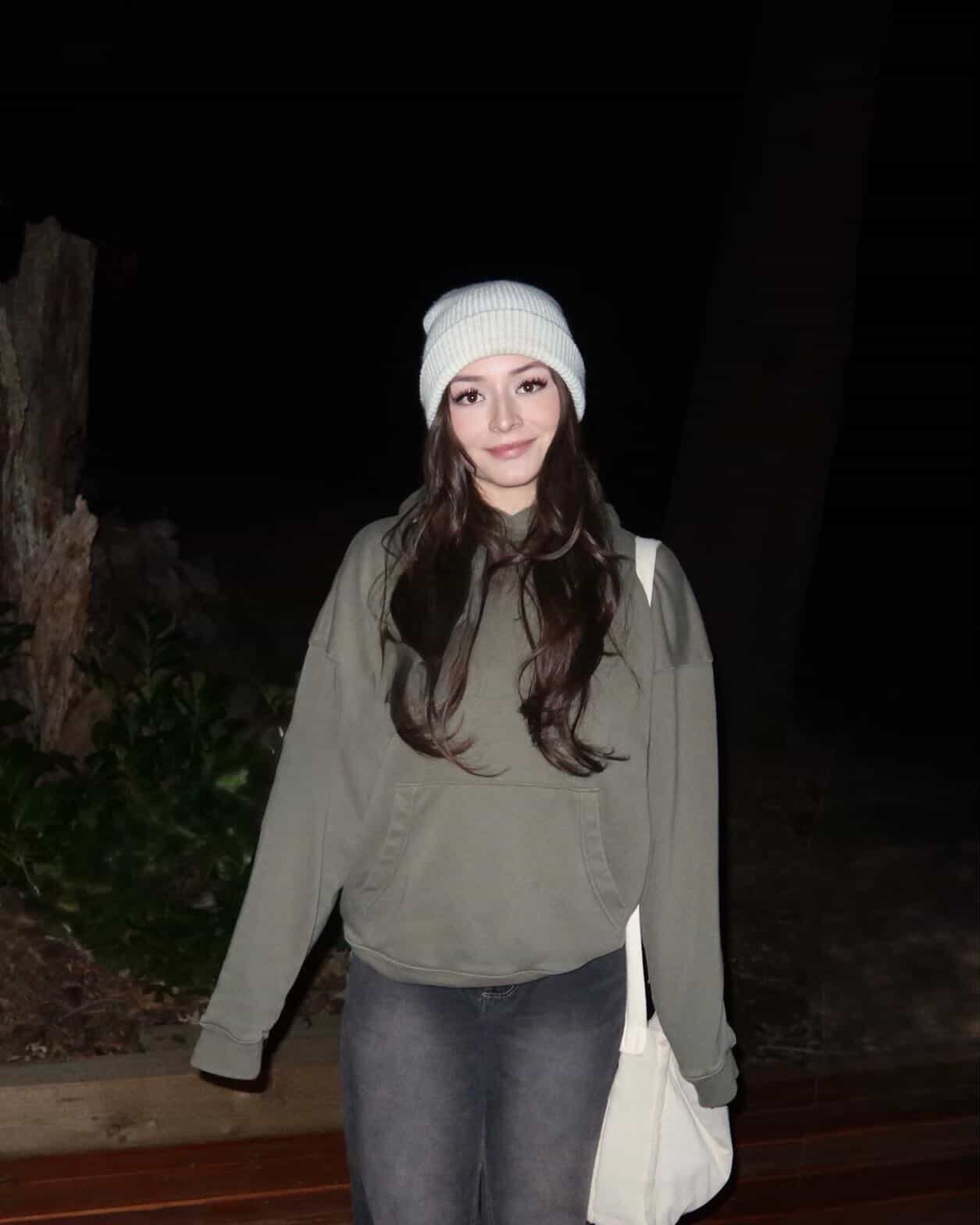 A woman wearing a green sweater and black jeans stands confidently, showcasing a casual yet stylish outfit