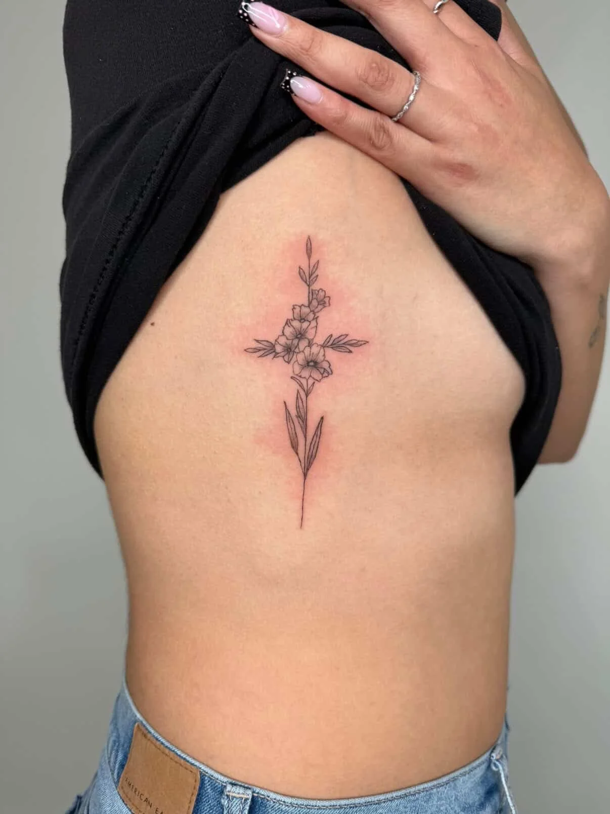 A tattoo of a delicate flower inked on the side of a woman's stomach, showcasing intricate details and vibrant colors