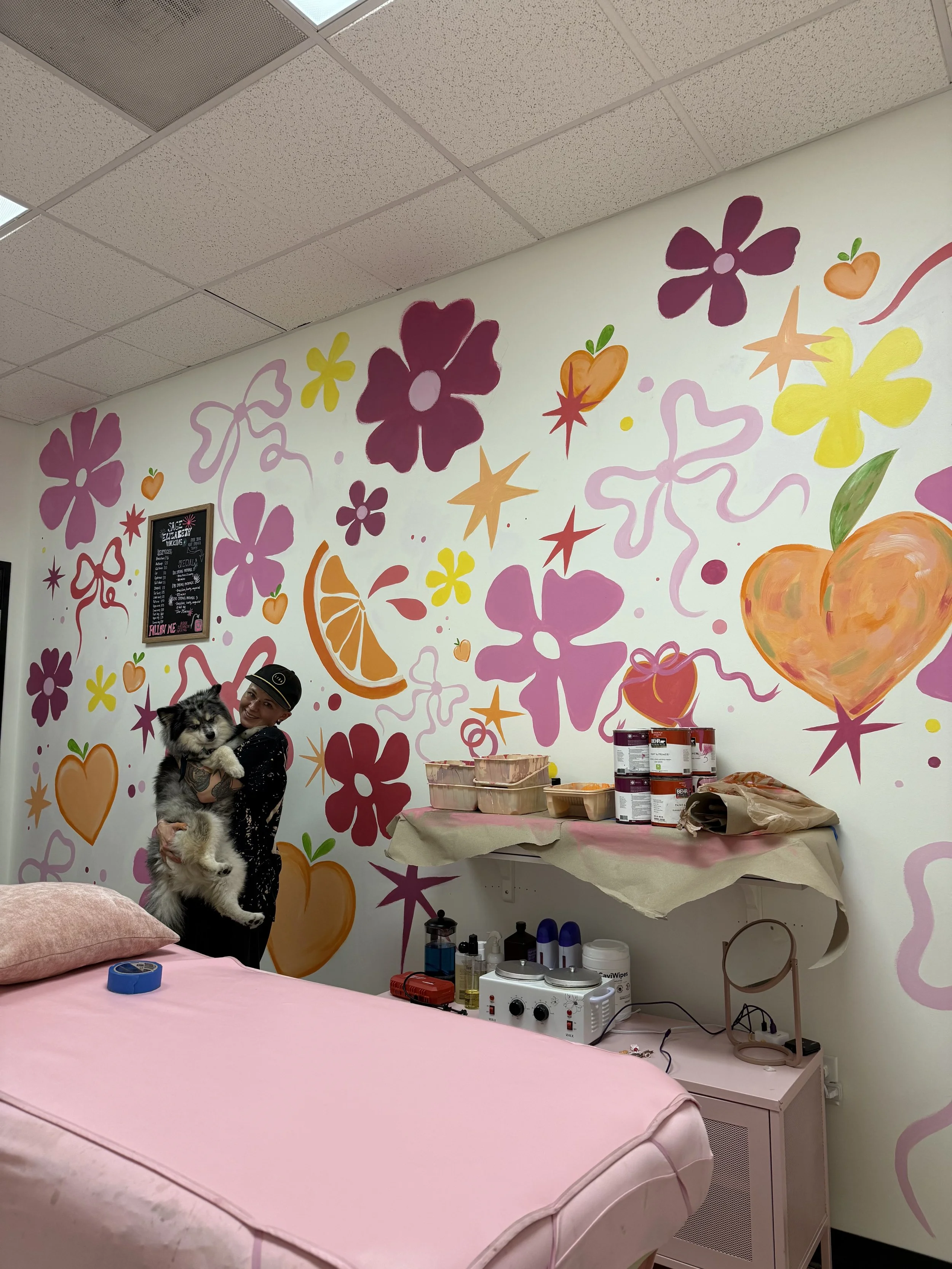 A woman holds a dog in a flower-painted room, showcasing a vibrant and cheerful atmosphere