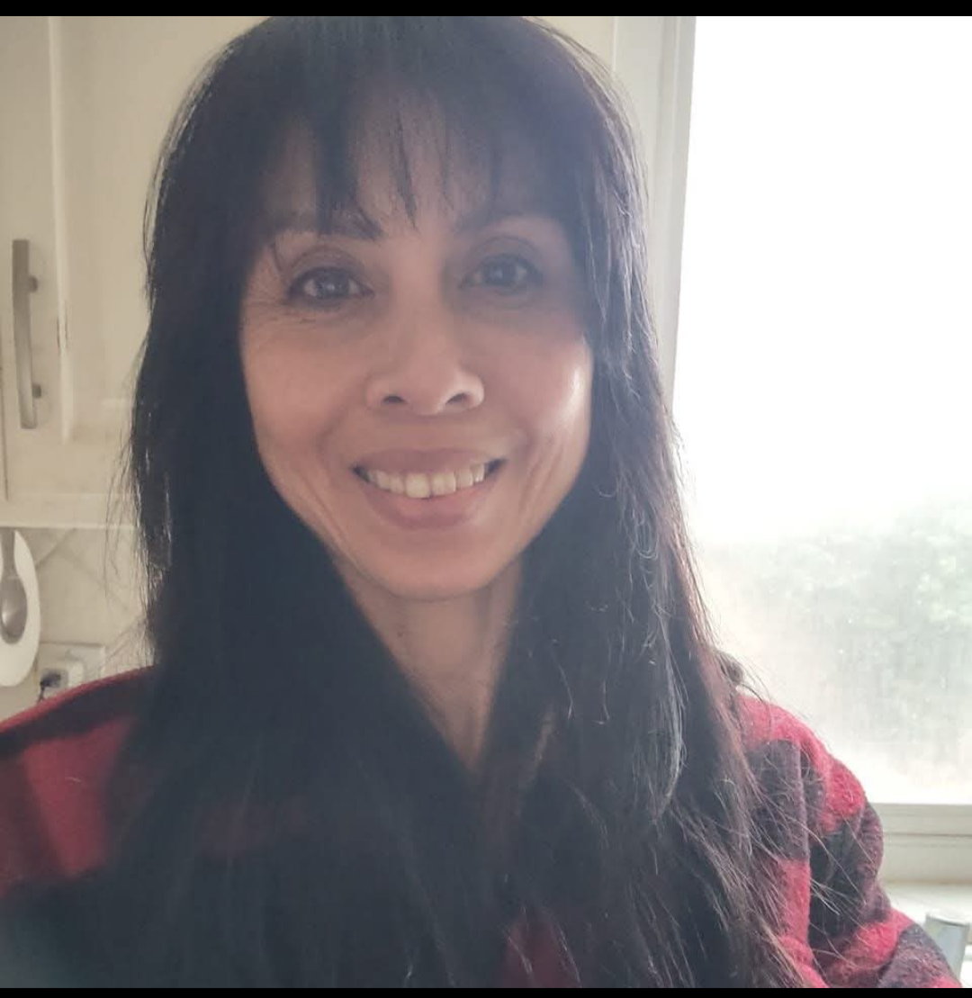 A woman with long black hair wearing a red plaid shirt stands confidently, showcasing her casual style.