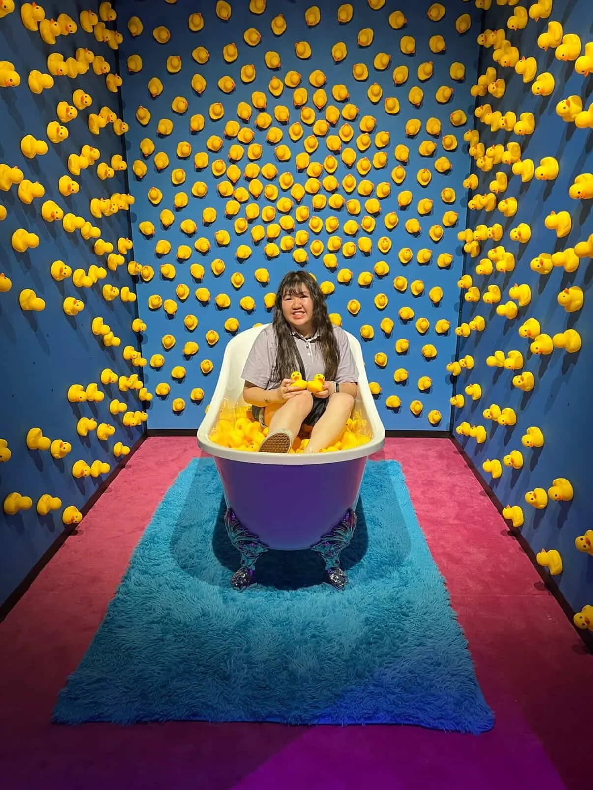 A woman relaxes in a bathtub filled with water, surrounded by cheerful yellow rubber ducks.