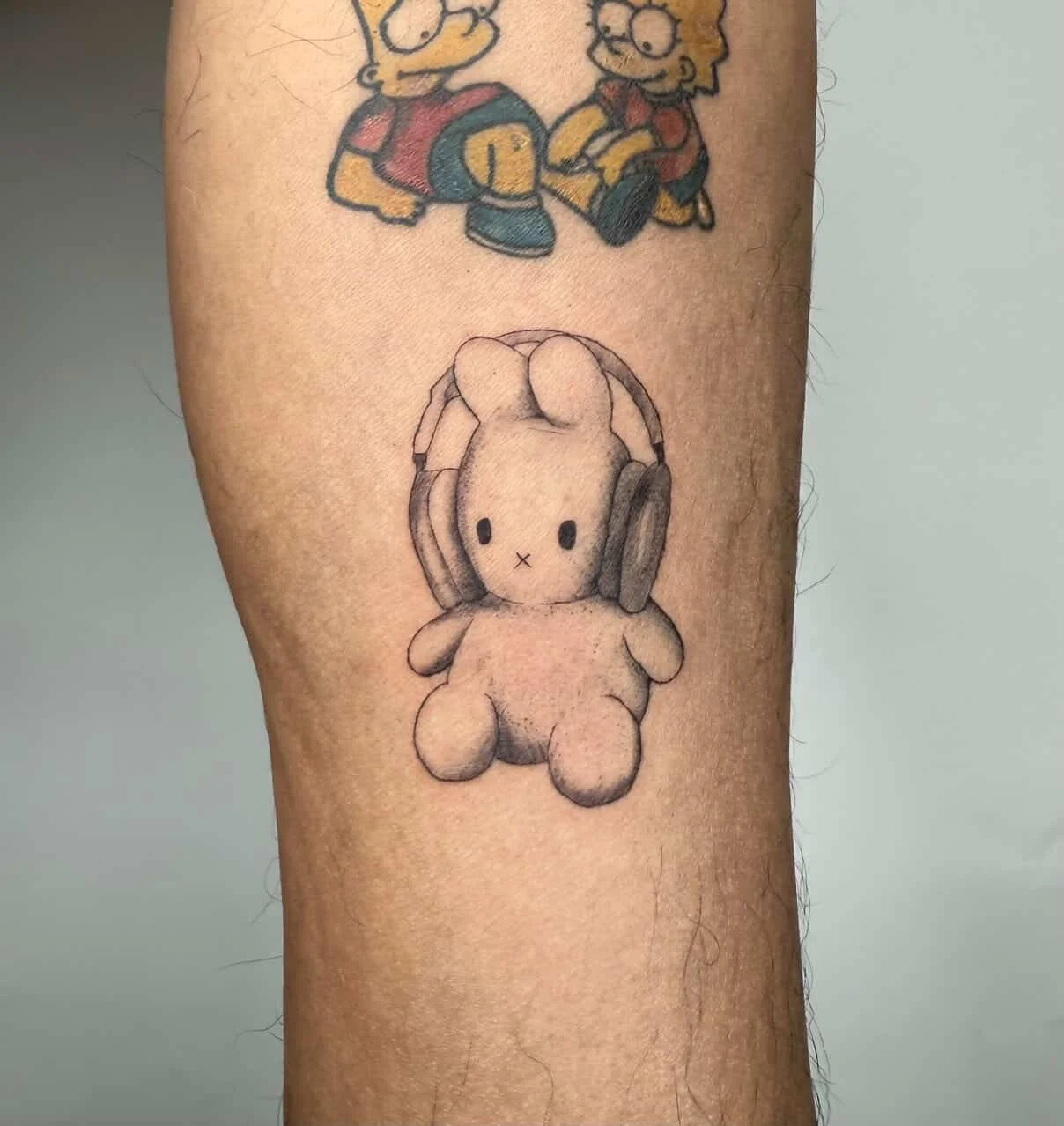 A tattoo of a teddy bear wearing headphones, located on a person's leg