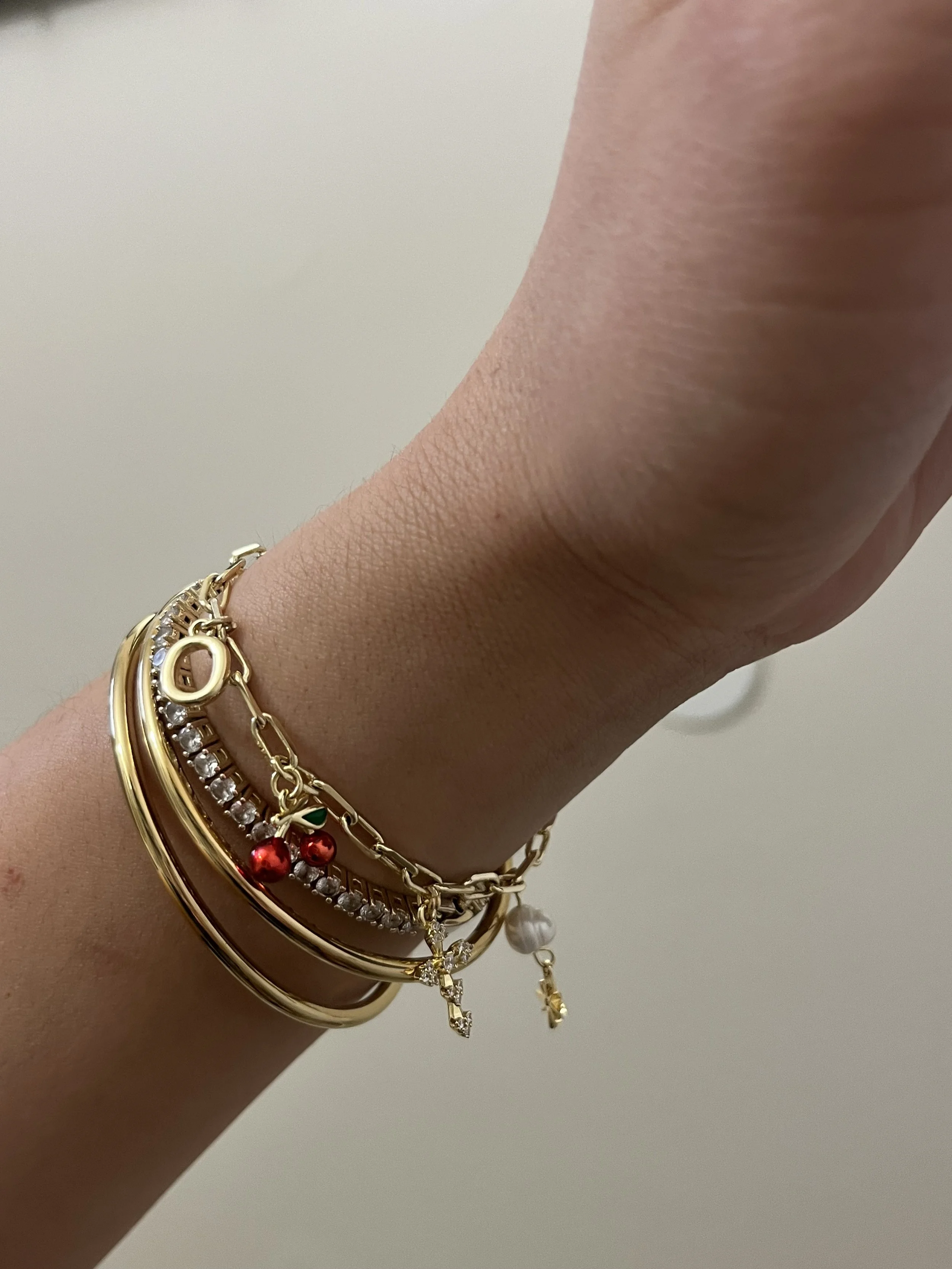 A person wearing a gold bracelet adorned with a red and white charm, showcasing a stylish accessory.