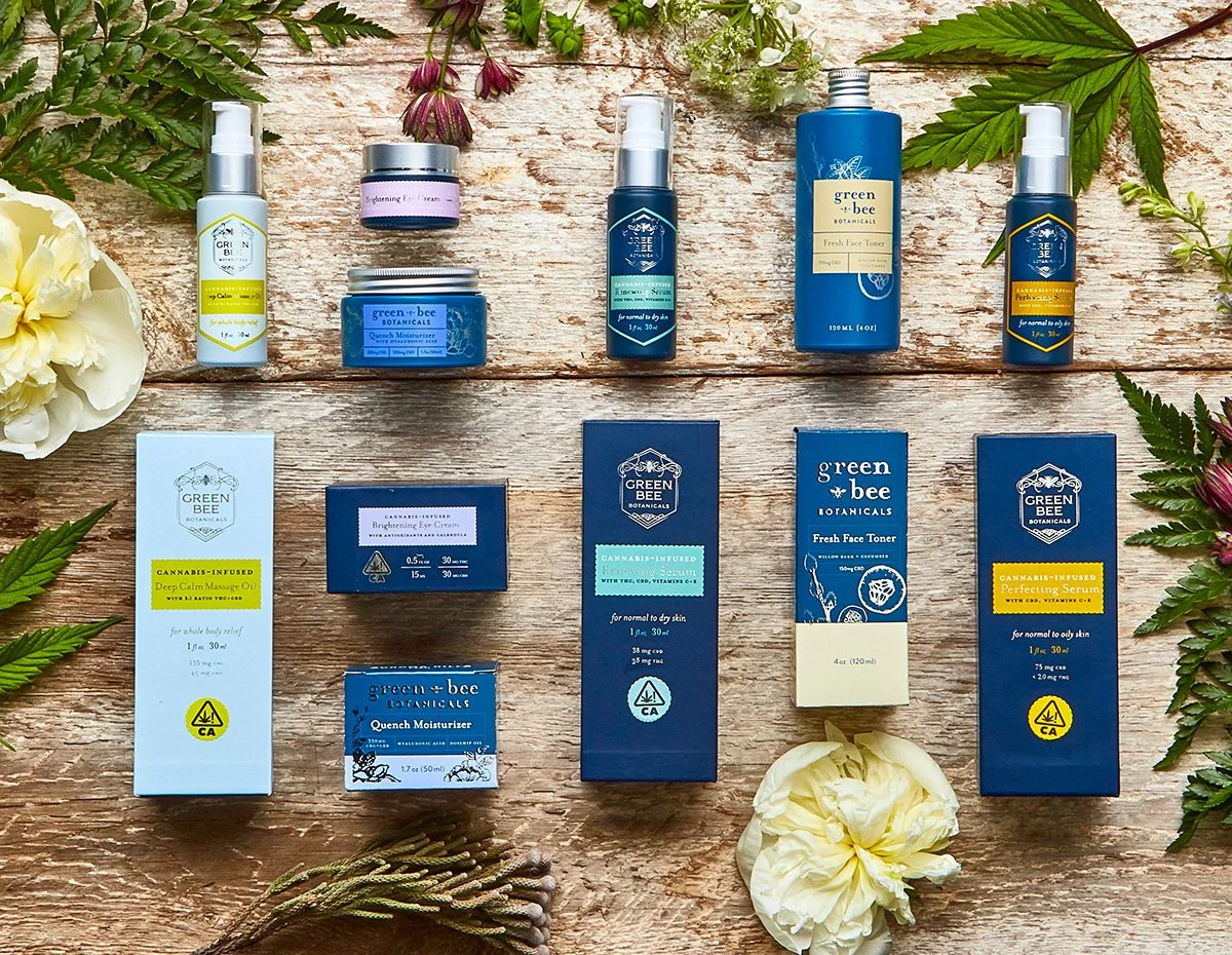 Collection of CBD and skincare products from Green Bee Botanicals arranged on a wooden surface with flowers and leaves for decoration.
