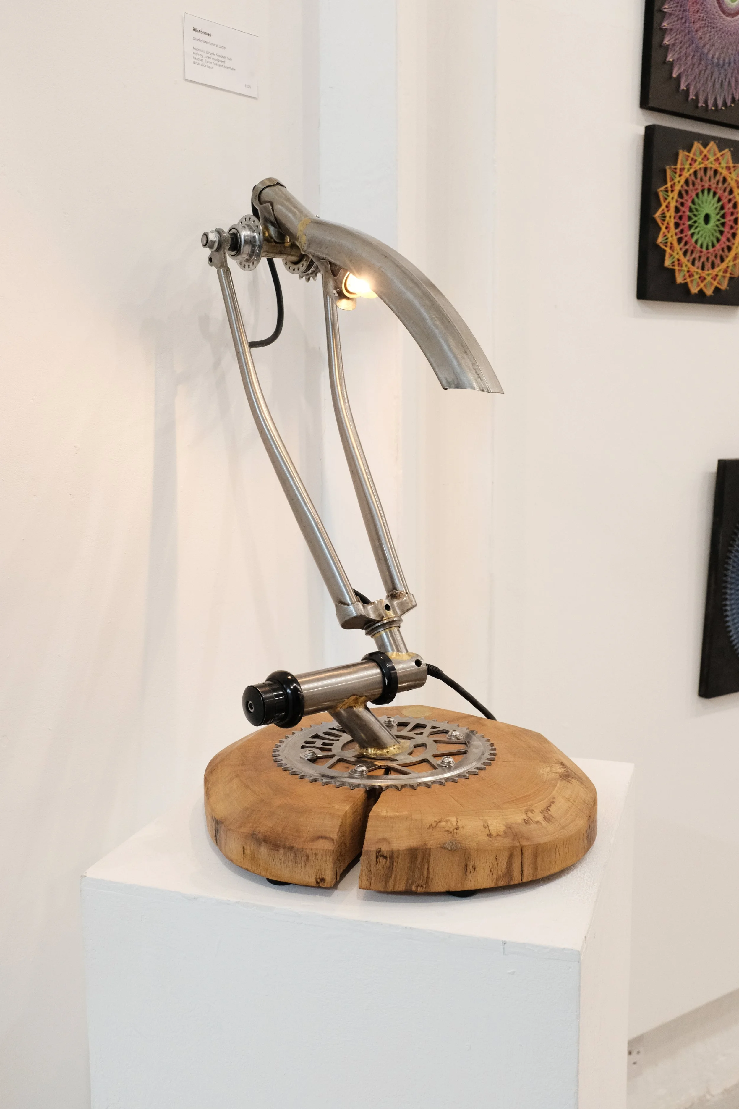 a mechanical desk lamp made of bicycle parts, mounted on a wood base.