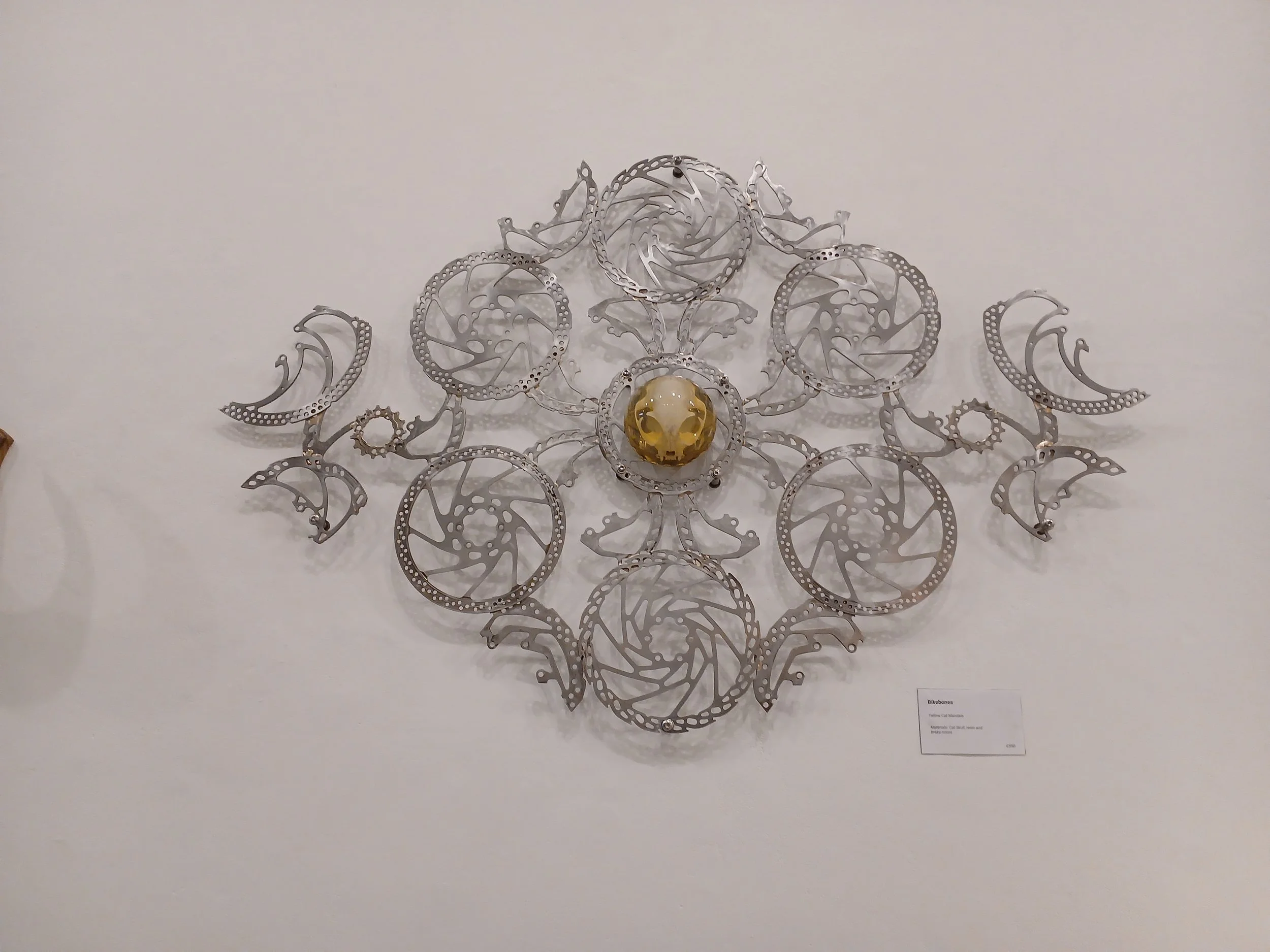 Wall-mounted sculpture made of metal discs arranged in a symmetrical pattern, surrounding a central golden sphere.