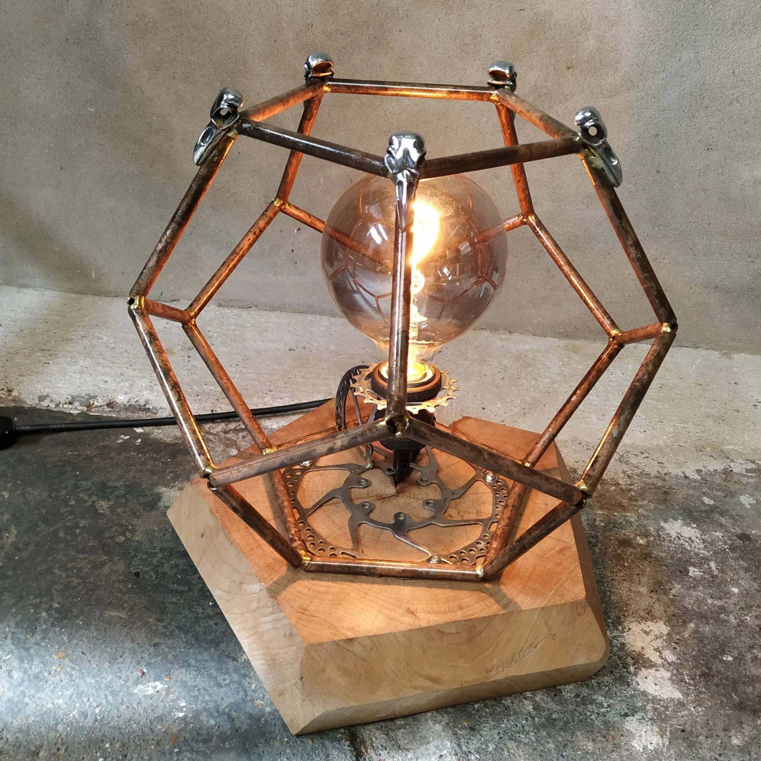 A steampunk-inspired table lamp with a copper pattina, crow skulls details mounted on a wooden base.