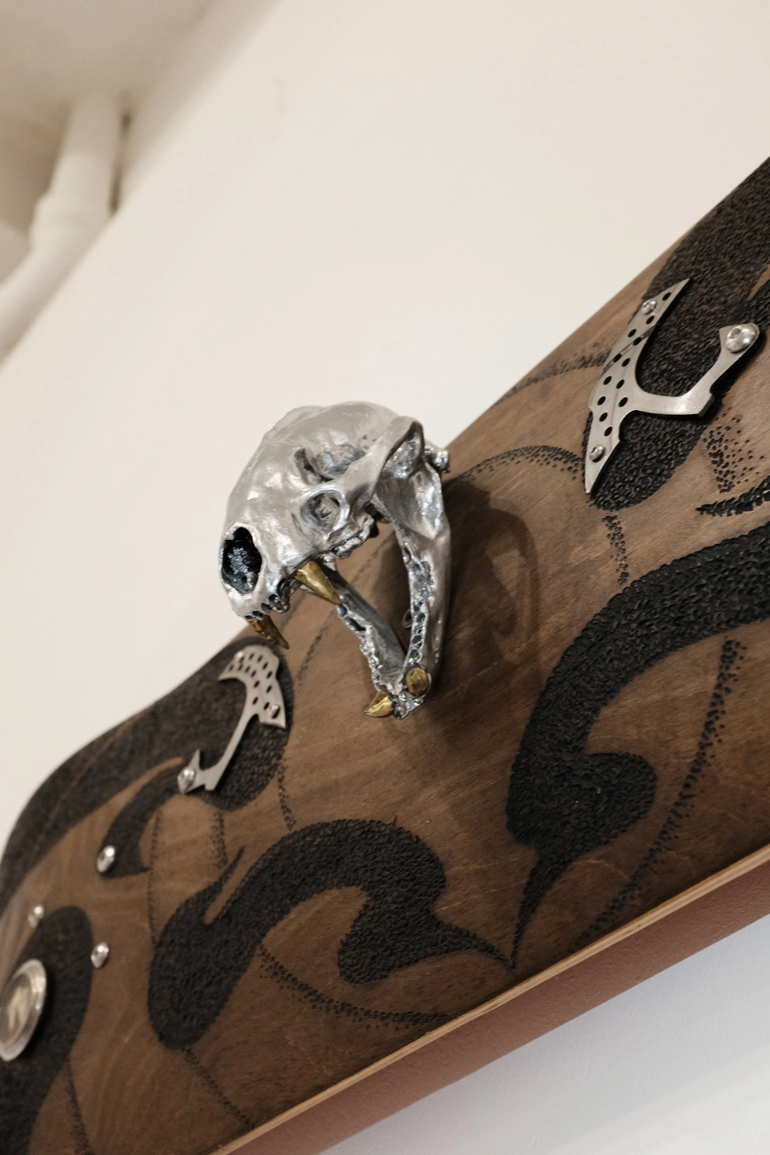 Decorative wooden skateboard with metallic skull and abstract metal embellishments.