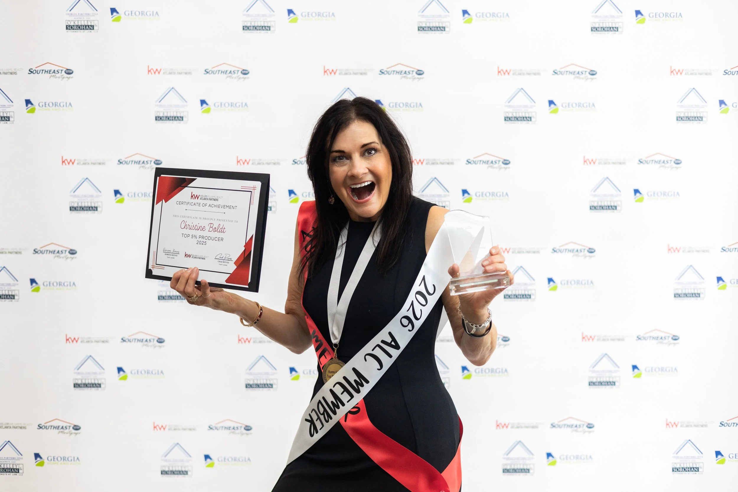 Woman celebrating on stage wearing a sash that reads '2022 ALVC MEMBER', holding a certificate of achievement and a glass award, smiling widely, backdrop with logos of Georgia, Southeast, and others.