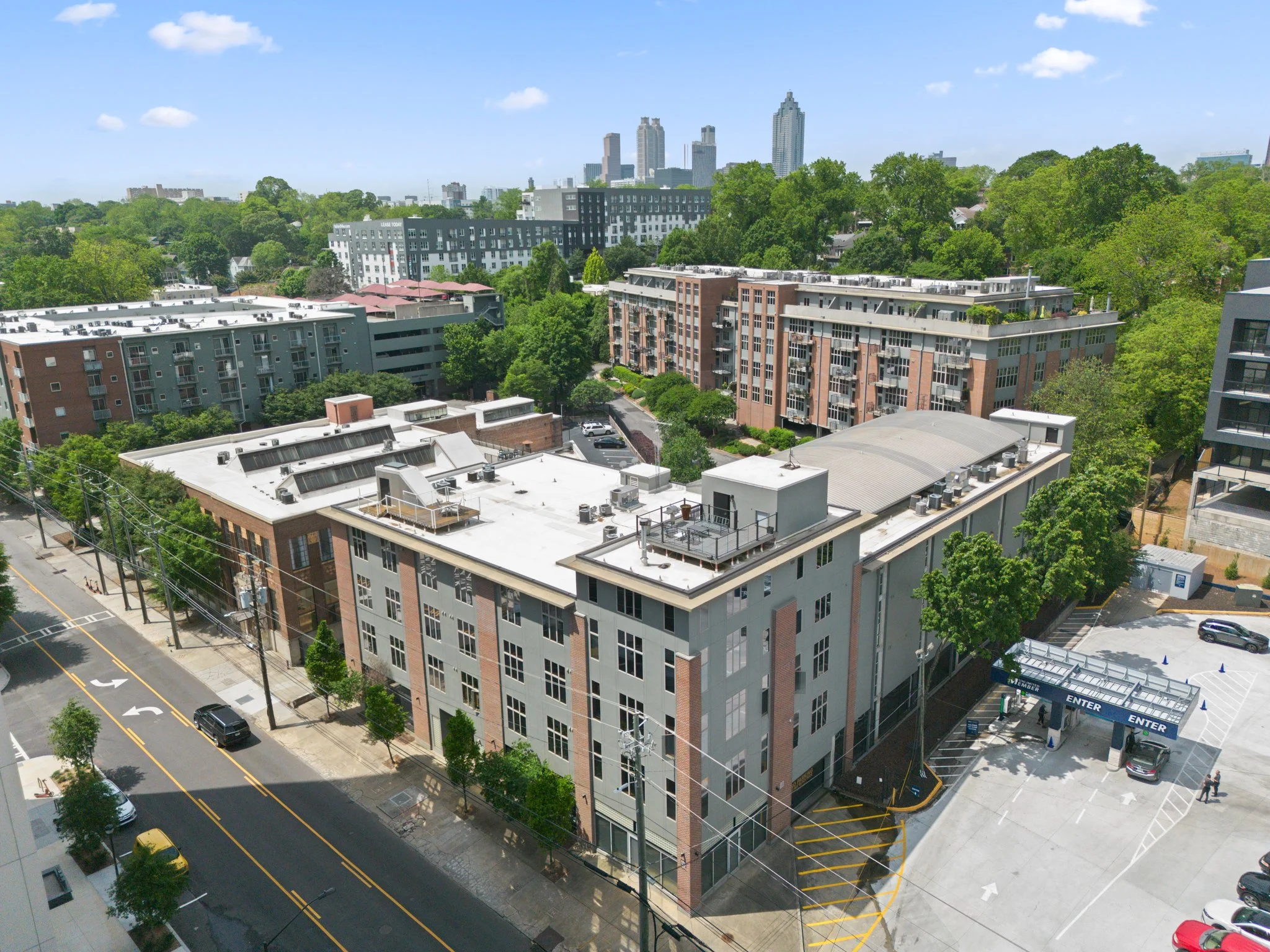 A cityscape view with a mix of modern apartment buildings and a distant skyline of tall skyscrapers under a partly cloudy sky, with green trees and streets below.