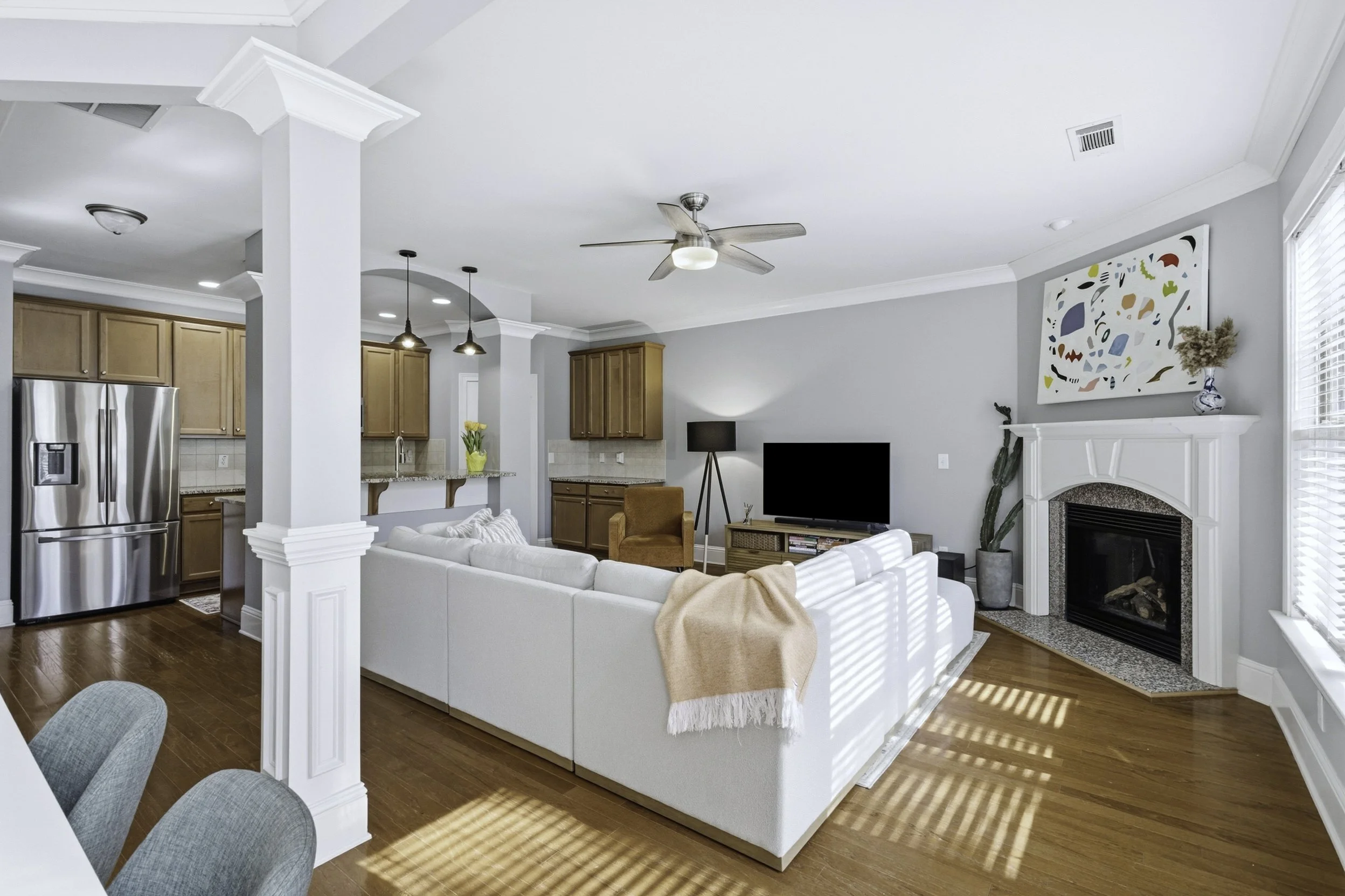 Living room with white sectional sofa, flat-screen TV, fireplace, hardwood floors, and large windows with blinds.