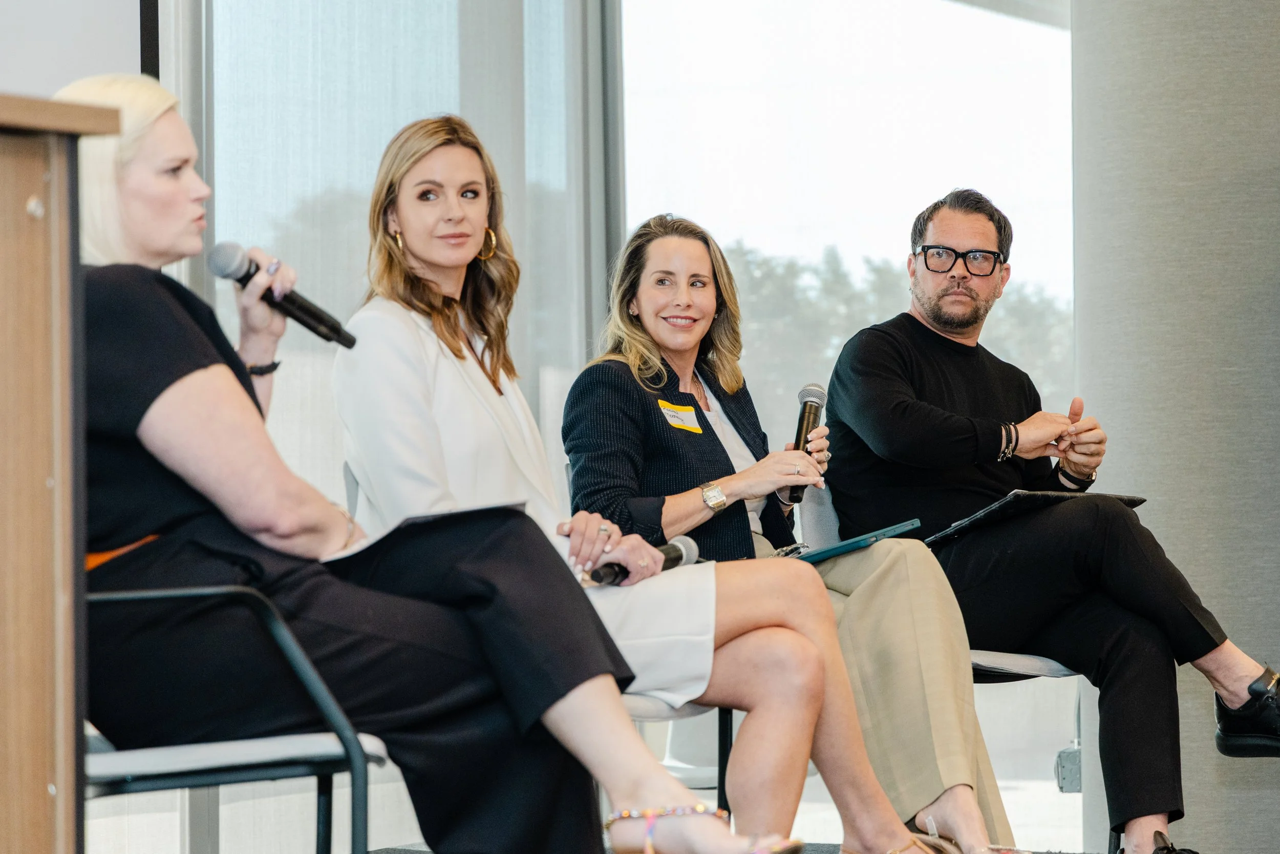 Four professionals sit on a panel during a discussion, with one woman speaking into a microphone, and the others listening and holding microphones.