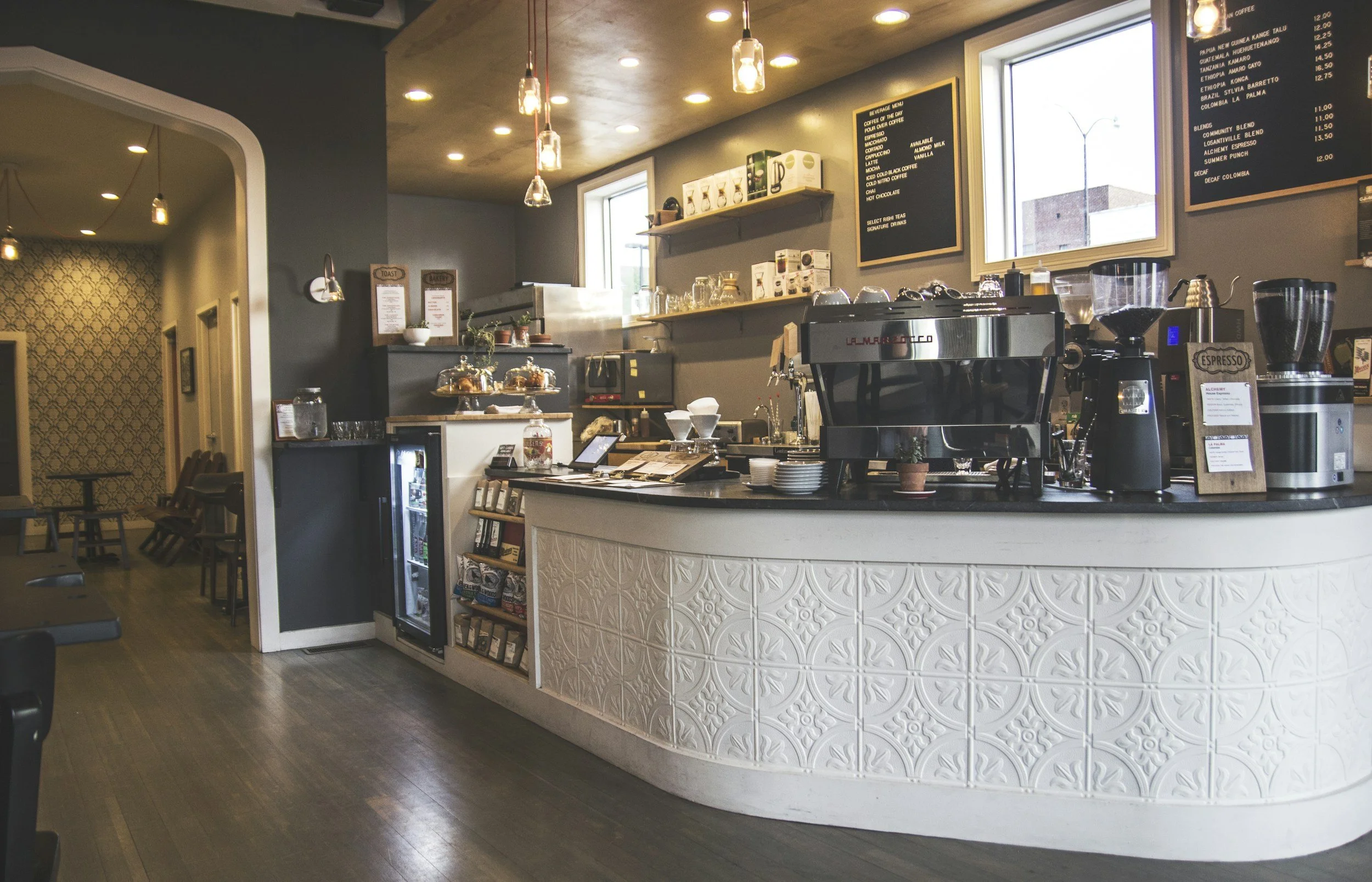 Interior of a modern coffee shop with a curved counter, coffee machines, menu boards, and seating area in the background.