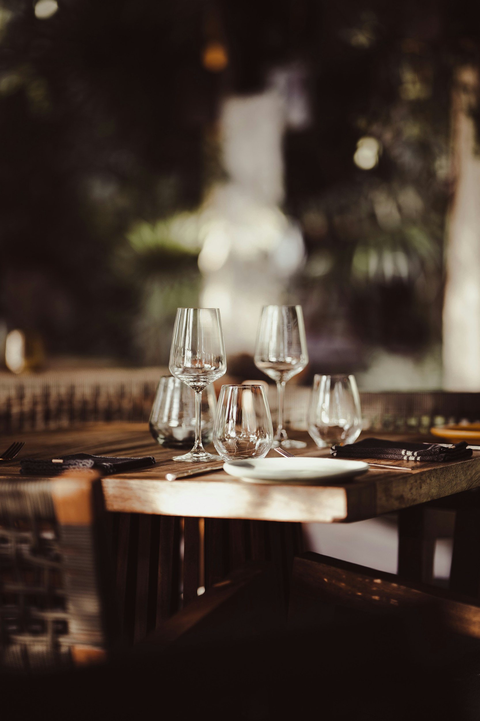 Empty restaurant table set with wine glasses, water glasses, and plates in warm lighting.
