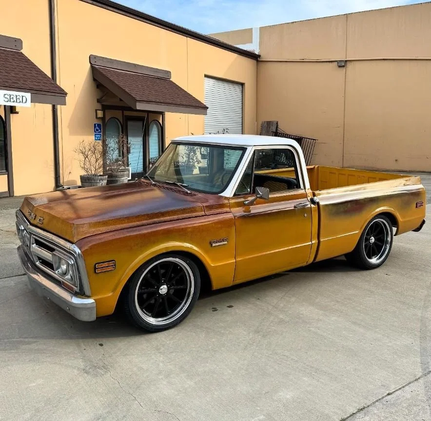 A vintage brown and white pickup truck parked outside a building with a yellow exterior.