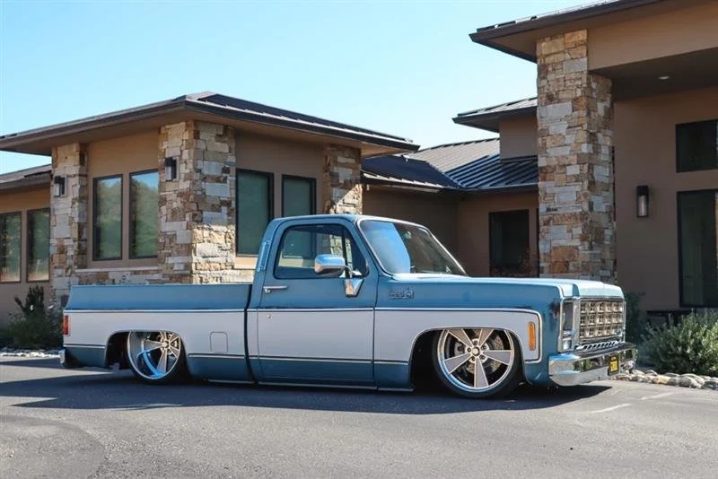 Custom lowered vintage pickup truck parked in front of a modern house with stone accents.