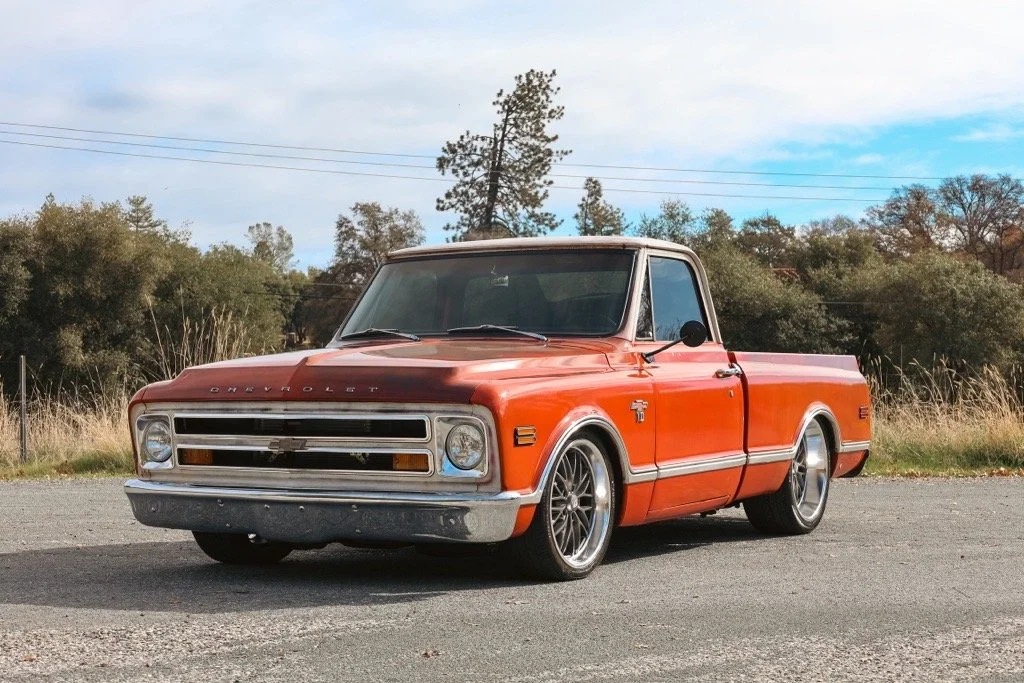 A vintage red Chevrolet pickup truck parked on an asphalt surface with trees and blue sky in the background.
