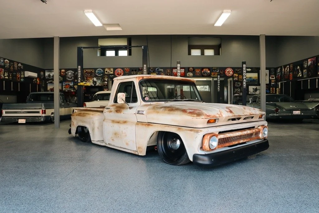 Rusty vintage pickup truck with lowered stance in a garage with other classic cars.