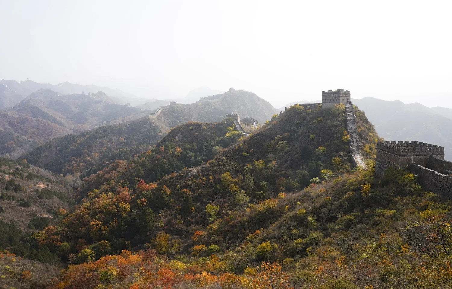 The Great Wall of China winding through mountains with autumn-colored trees.