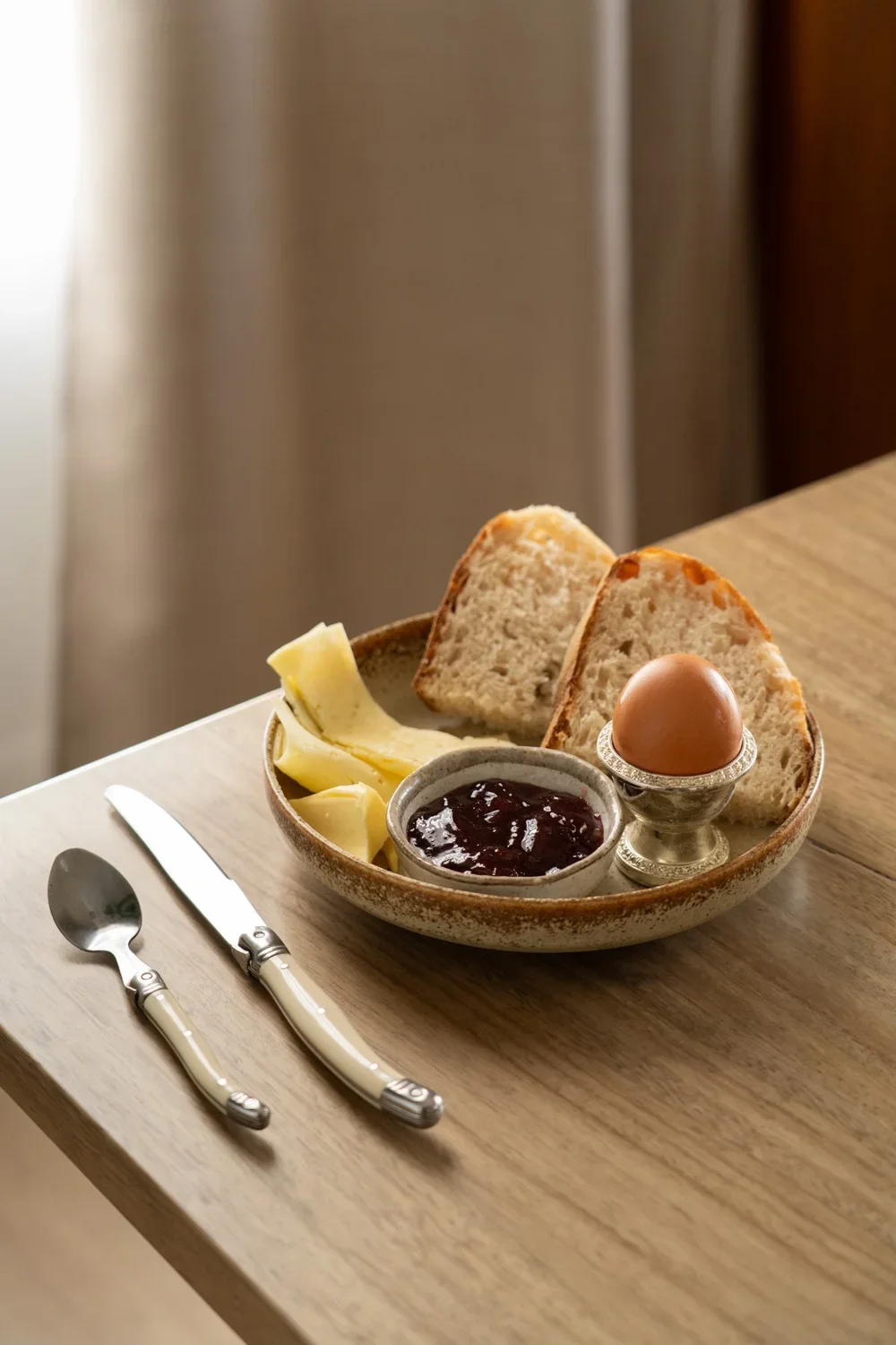 Boiled egg, bread and cheese on plate sitting on table with cutlery
