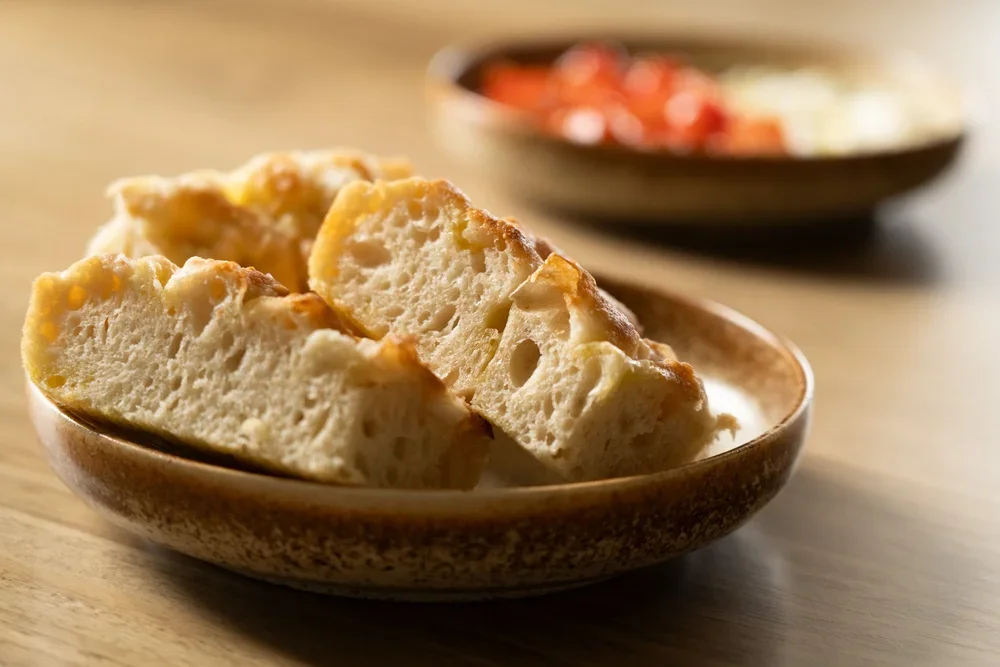 Close-up of bread slices in a shallow bowl with a bowl of tomatoes in the background.