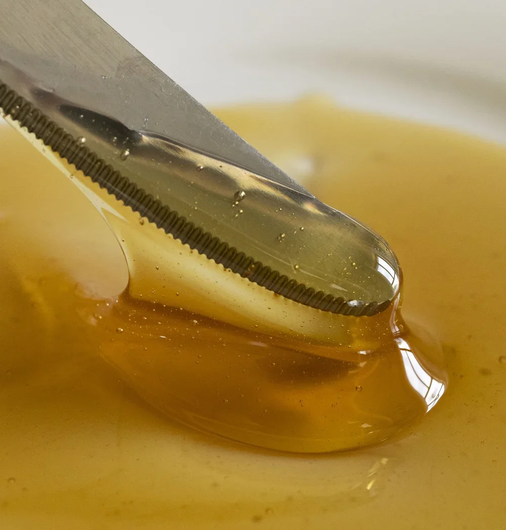 Close-up of a knife scooping honey from a container with honey dripping off the spoon.