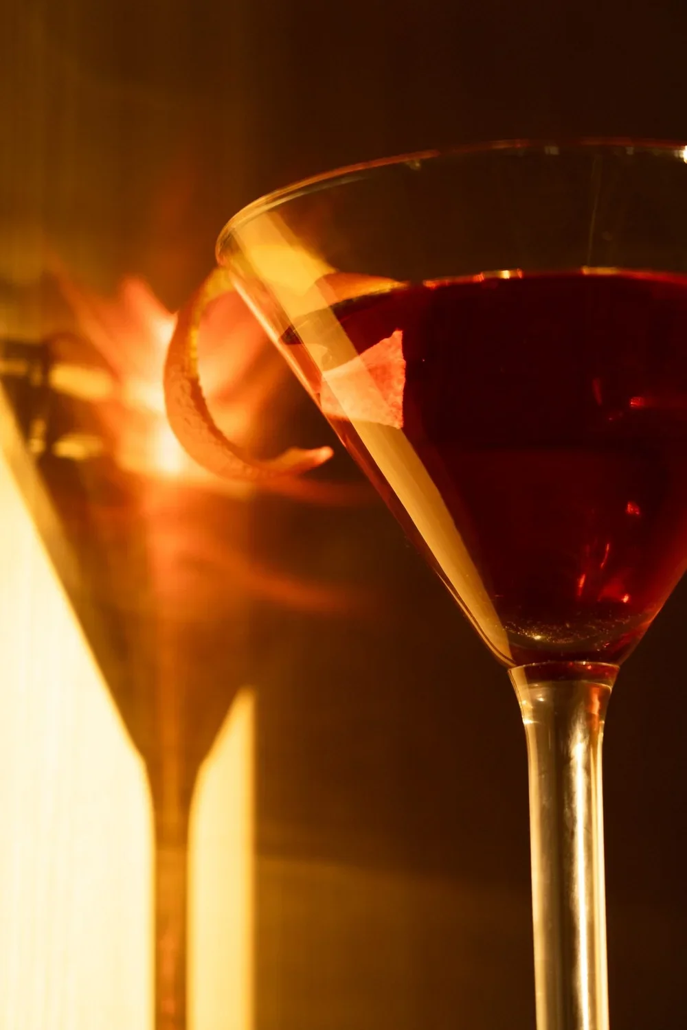 A close-up of a glass of red wine with a lemon slice on the rim, with warm lighting creating reflections and shadows.