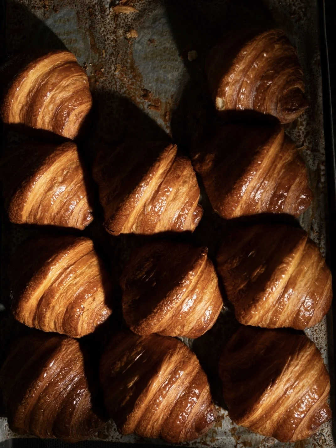 A tray of freshly baked croissants with golden brown, flaky, layered pastry.