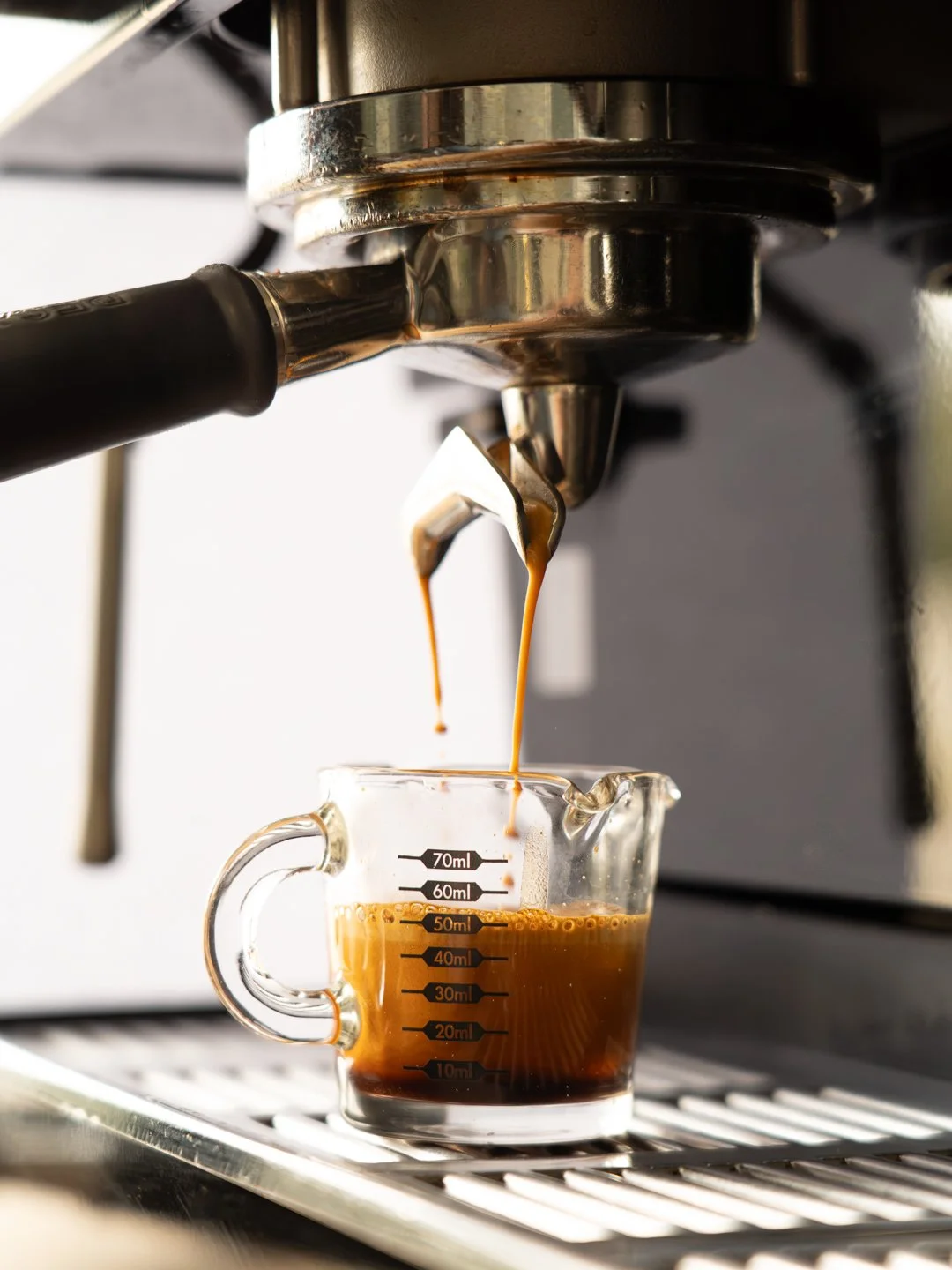 Small glass cup sitting in coffee machine with espresso dripping into it